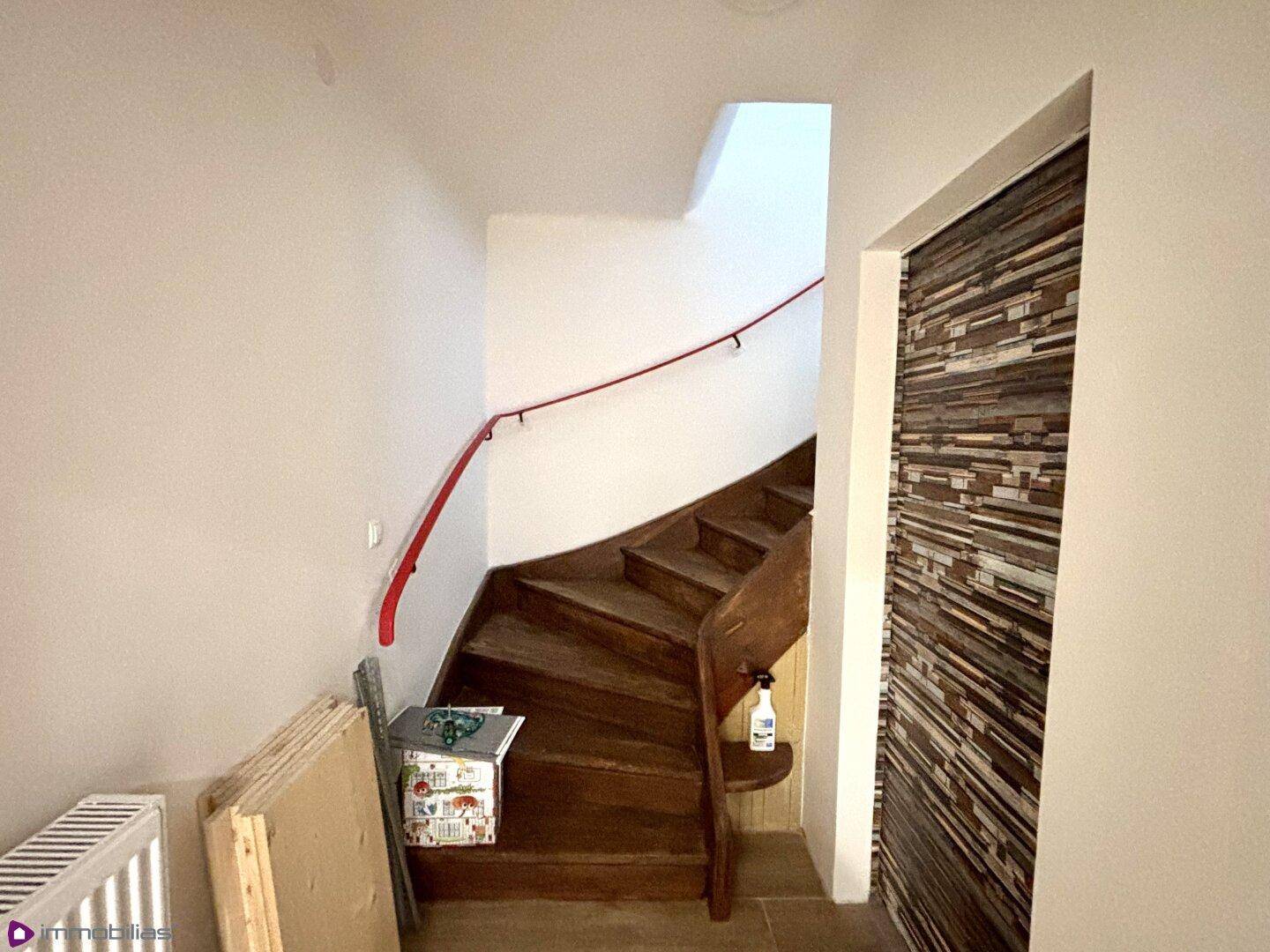 Holztreppe mit rotem Handlauf, die in die obere Etage führt.