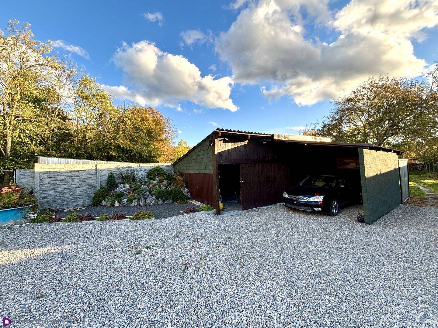 Außenansicht des Carports und eines Steingartens unter blauem Himmel.