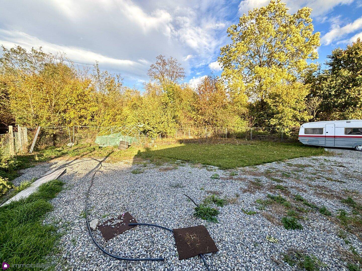 Grünfläche mit Bäumen, Kiesweg und einem Wohnwagen im Hintergrund.