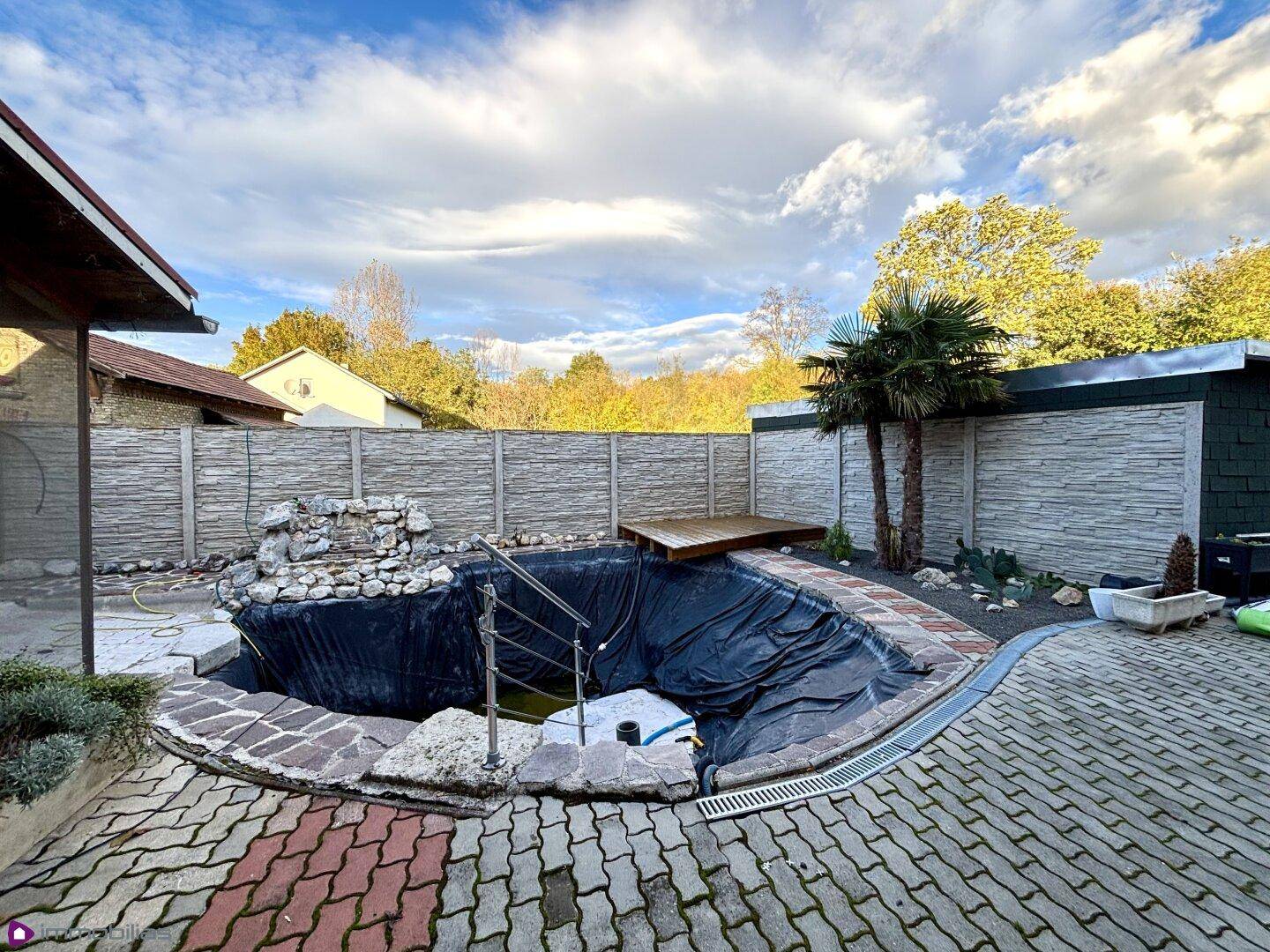 Garten mit einem Teich in Bau, gepflastertem Bereich und Palmen.