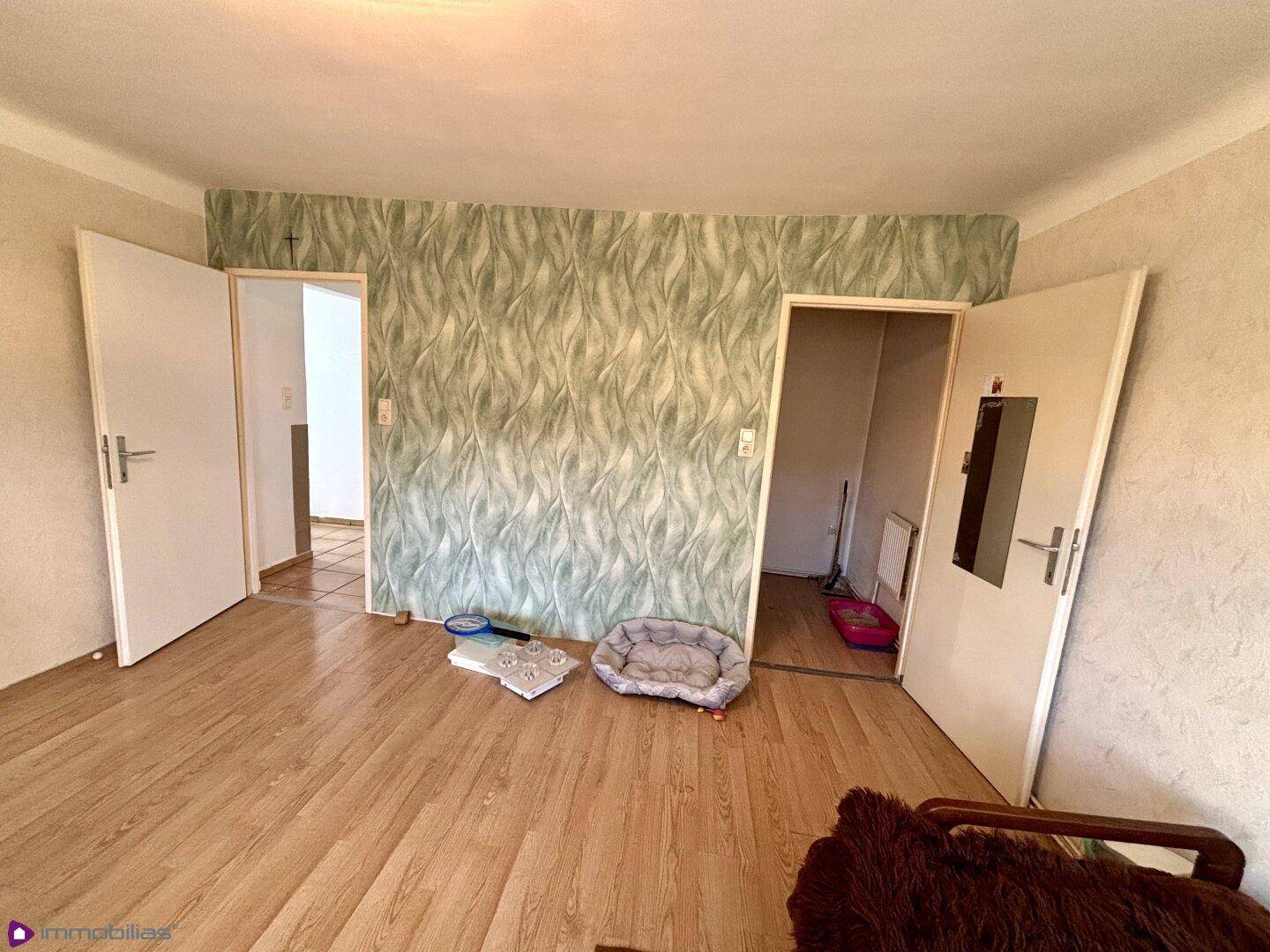 Raum mit Laminatboden und grüner Mustertapete, der zu weiteren Zimmern führt.