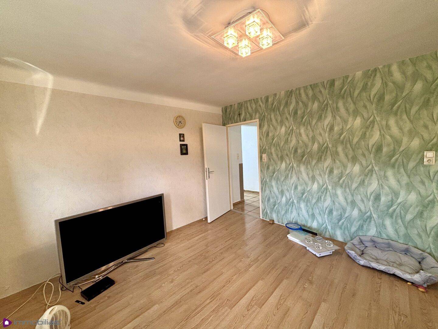 Heller Raum mit Laminatboden, Fernseher und grüner Mustertapete.