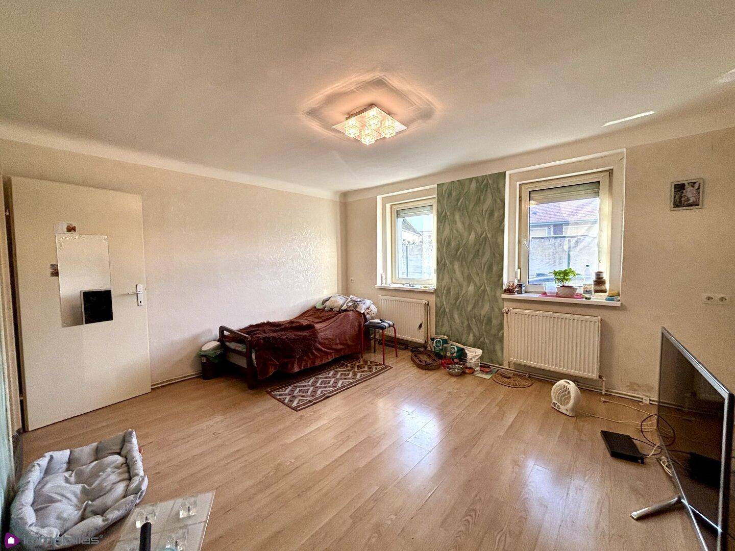 Schlafzimmer mit Laminatboden, zwei Fenstern und einem Bett.