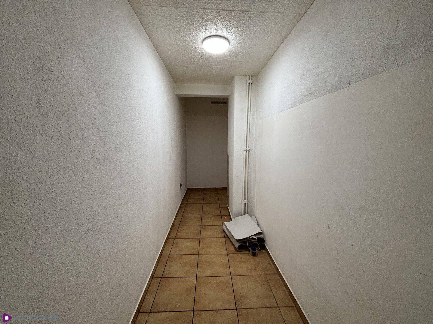 Schmaler Flur mit Fliesenboden und schlichten weißen Wänden.