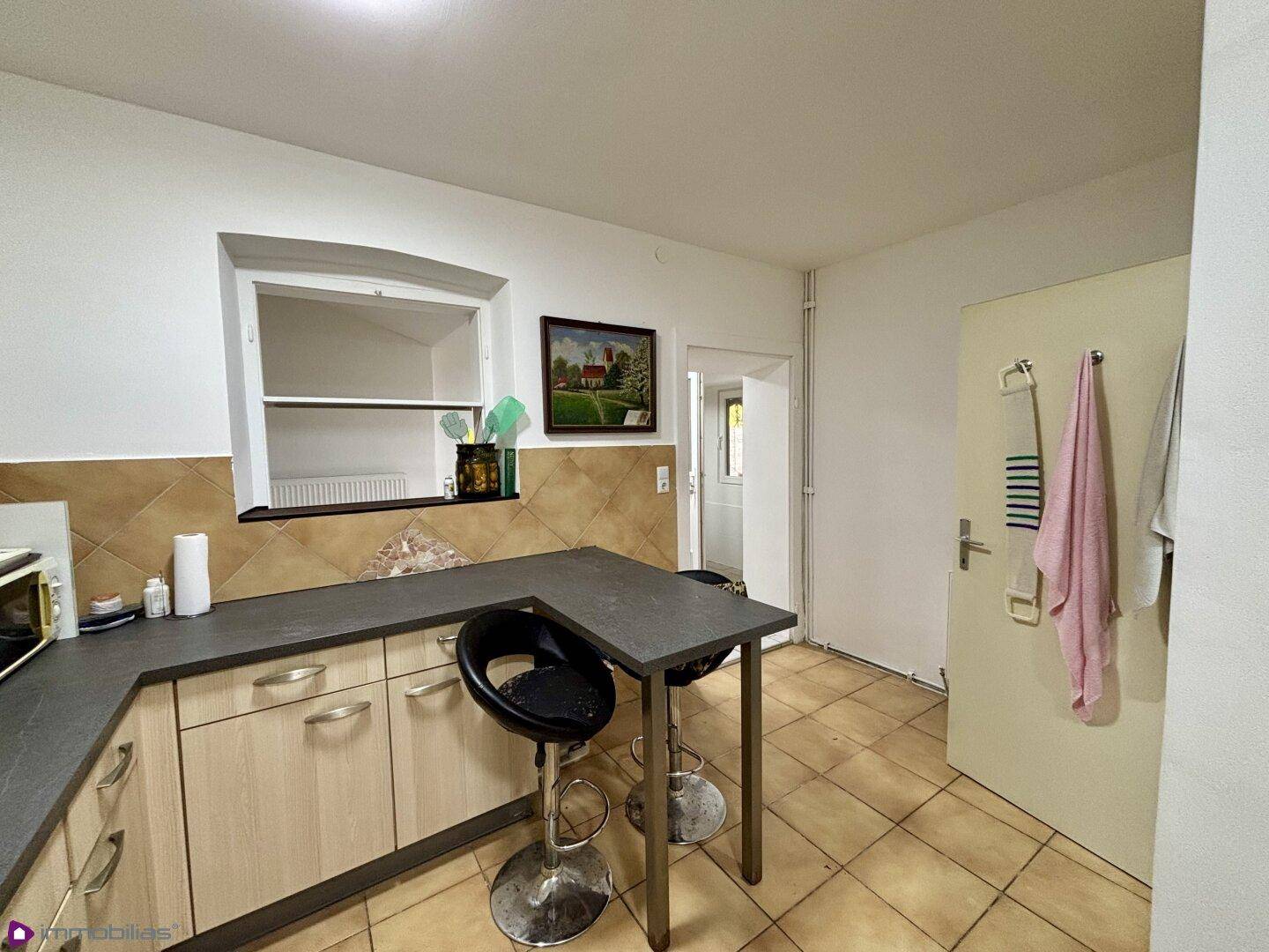 Küche mit Frühstücksbar, hellen Holzschränken und Fliesenboden.