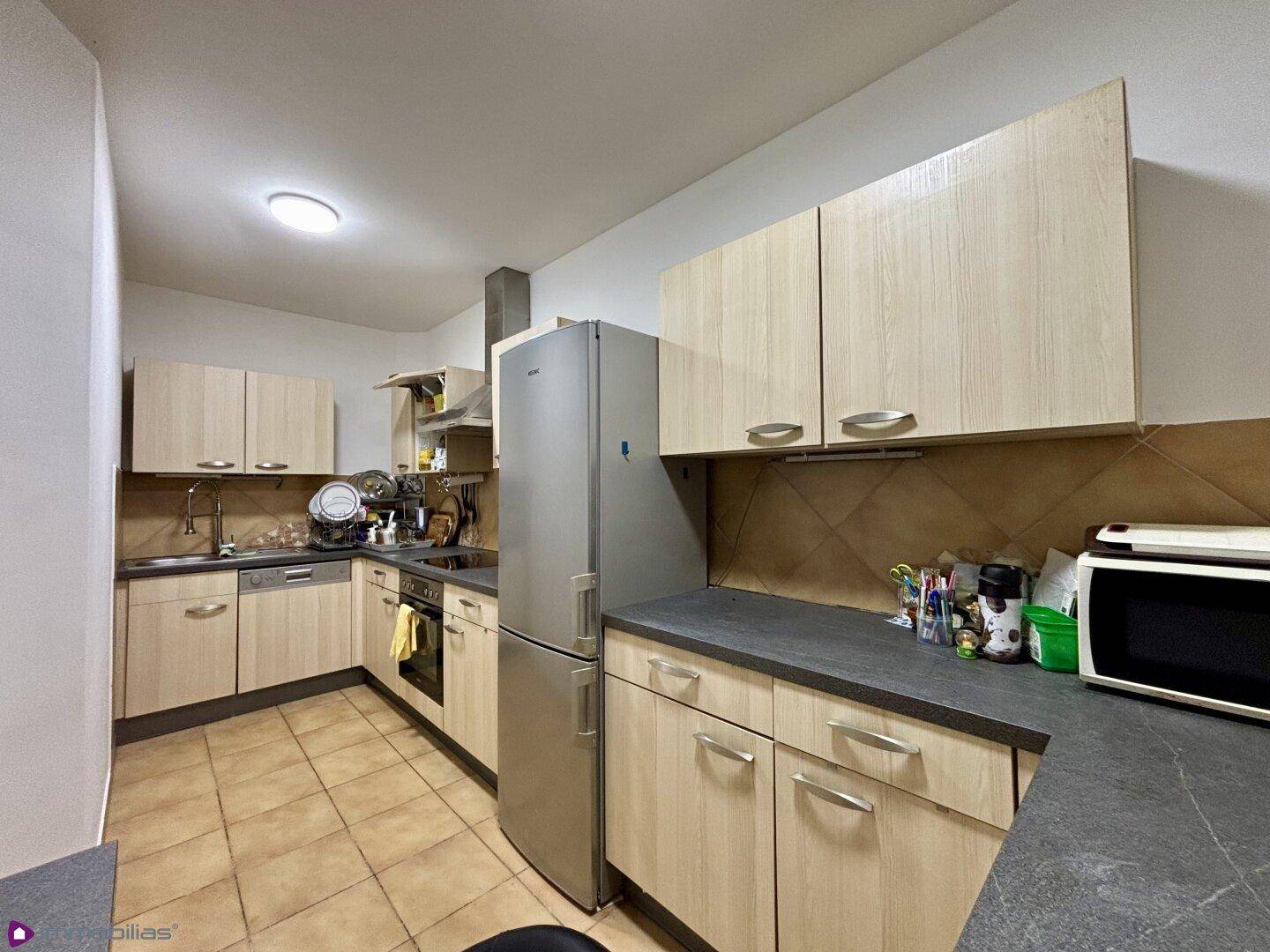 Küche mit hellen Holzschränken, dunklen Arbeitsplatten und modernen Geräten.