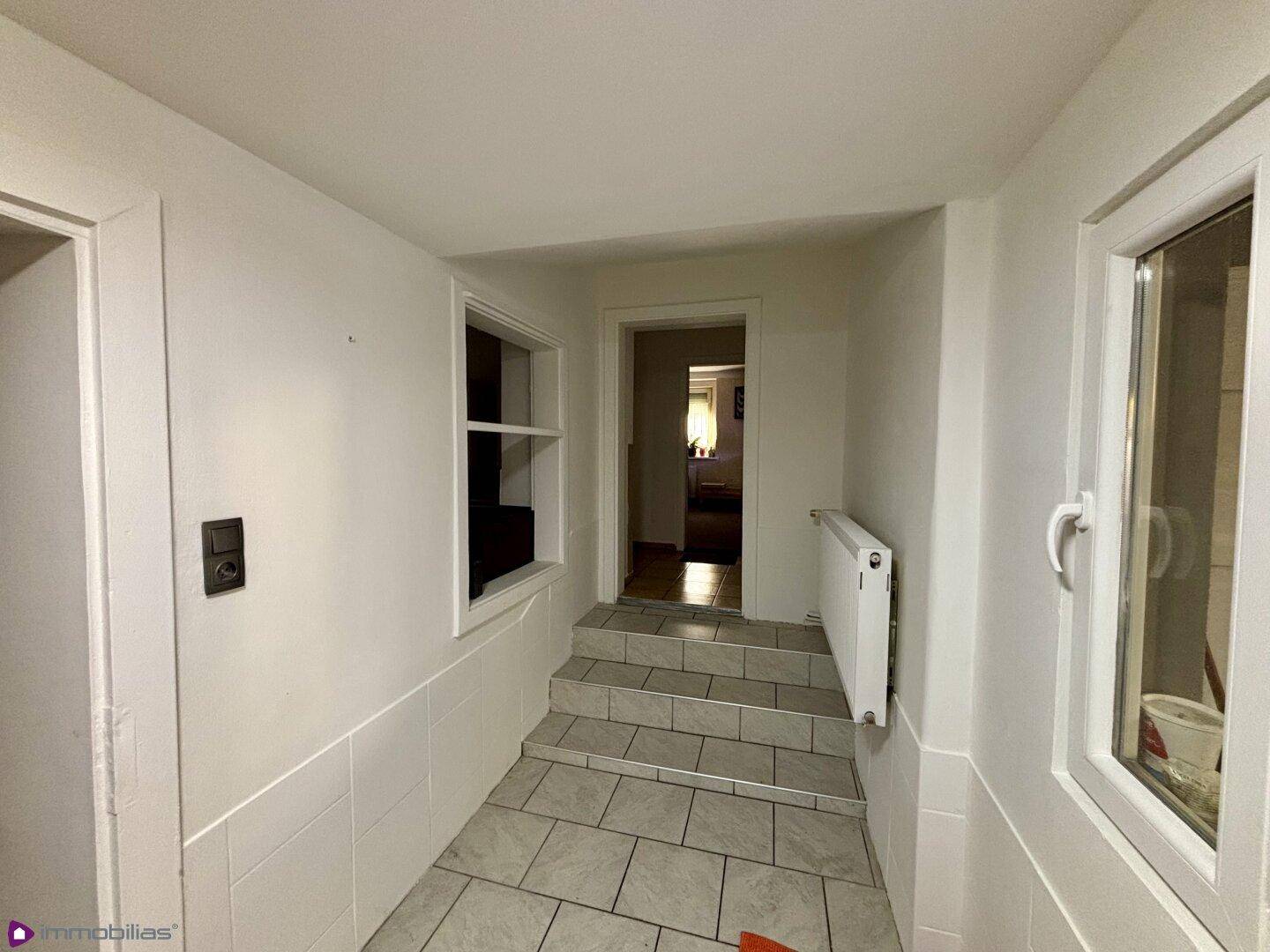 Flur mit gefliesten Stufen und Fenstern, die für Helligkeit sorgen.