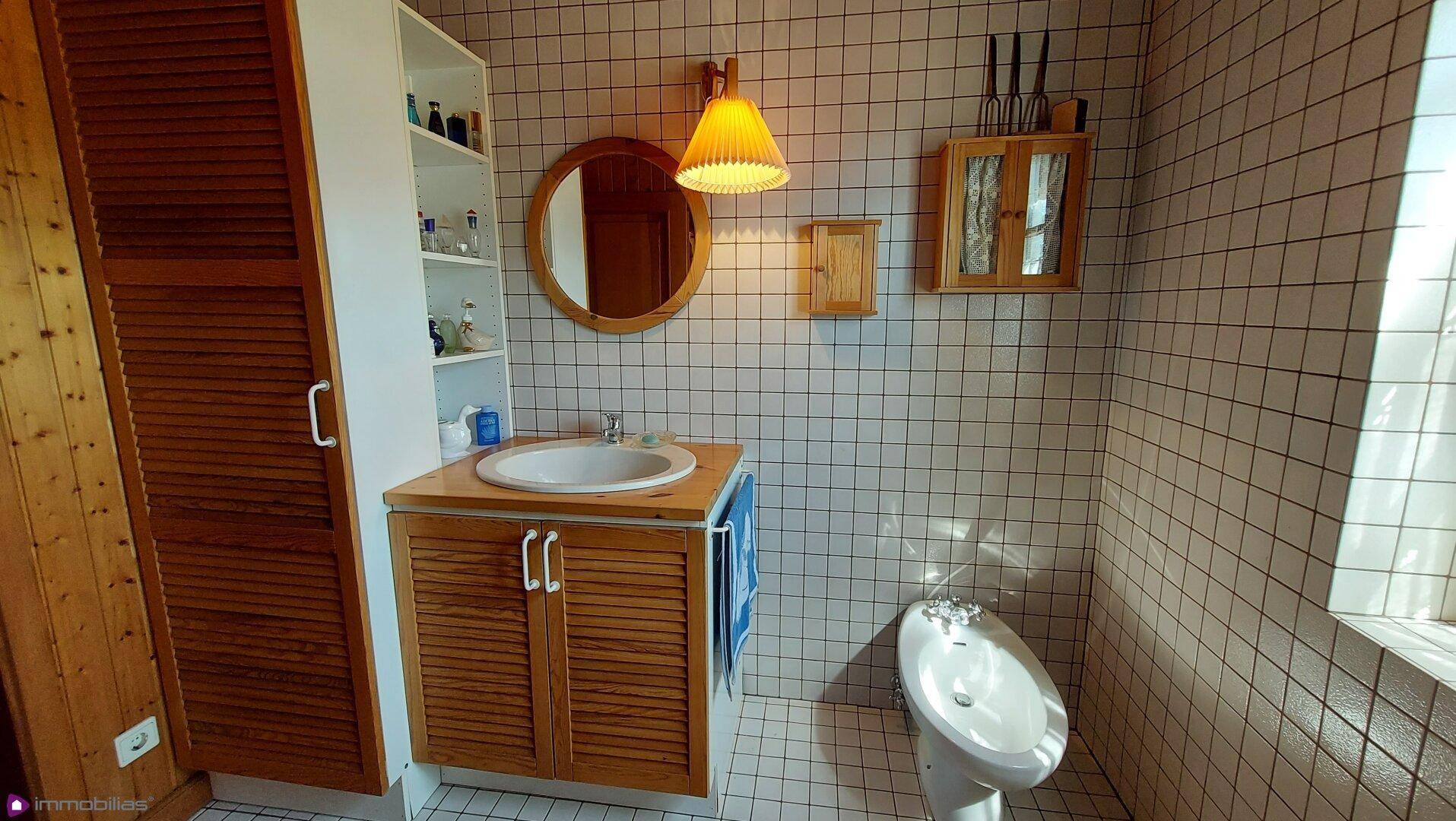 Badezimmer mit Waschbecken, Bidet und Holzschränken, sauber und hell gefliest.
