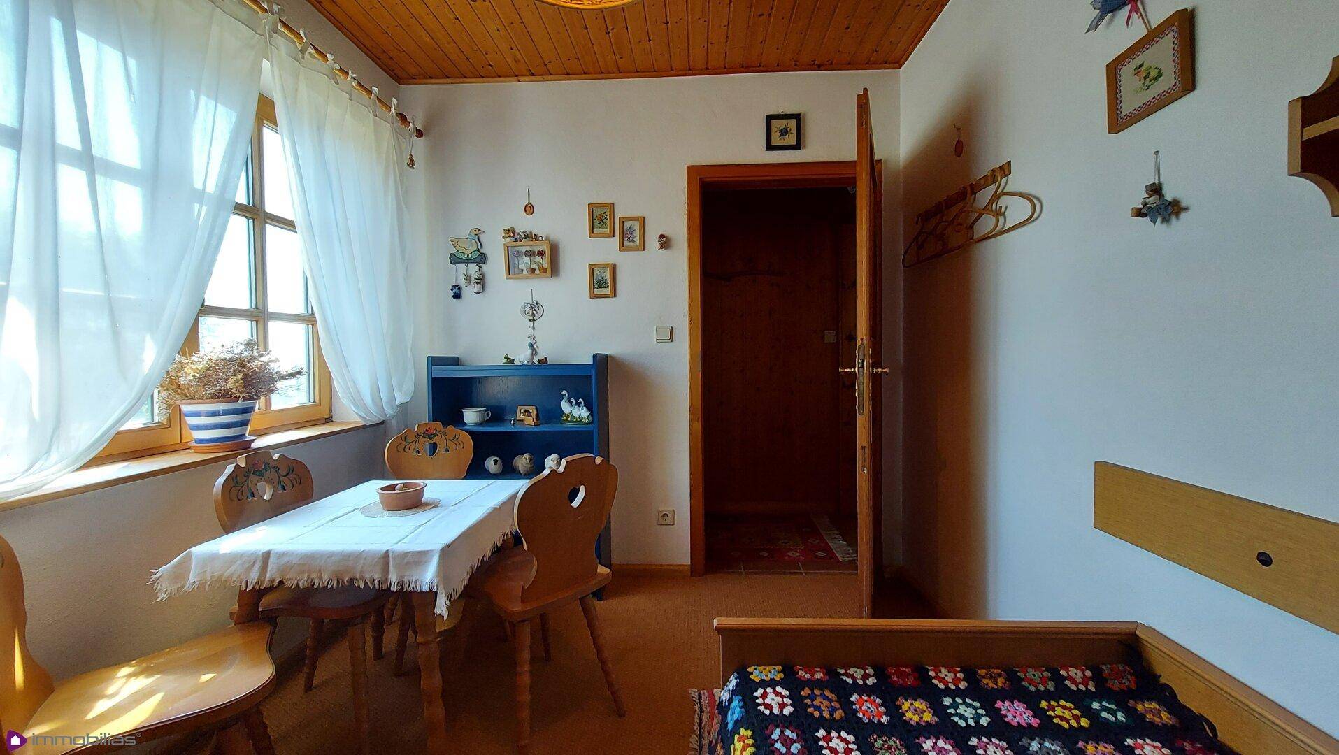 Helles Gästezimmer mit Einzelbett, Esstisch und Blick ins Grüne durch große Fenster.