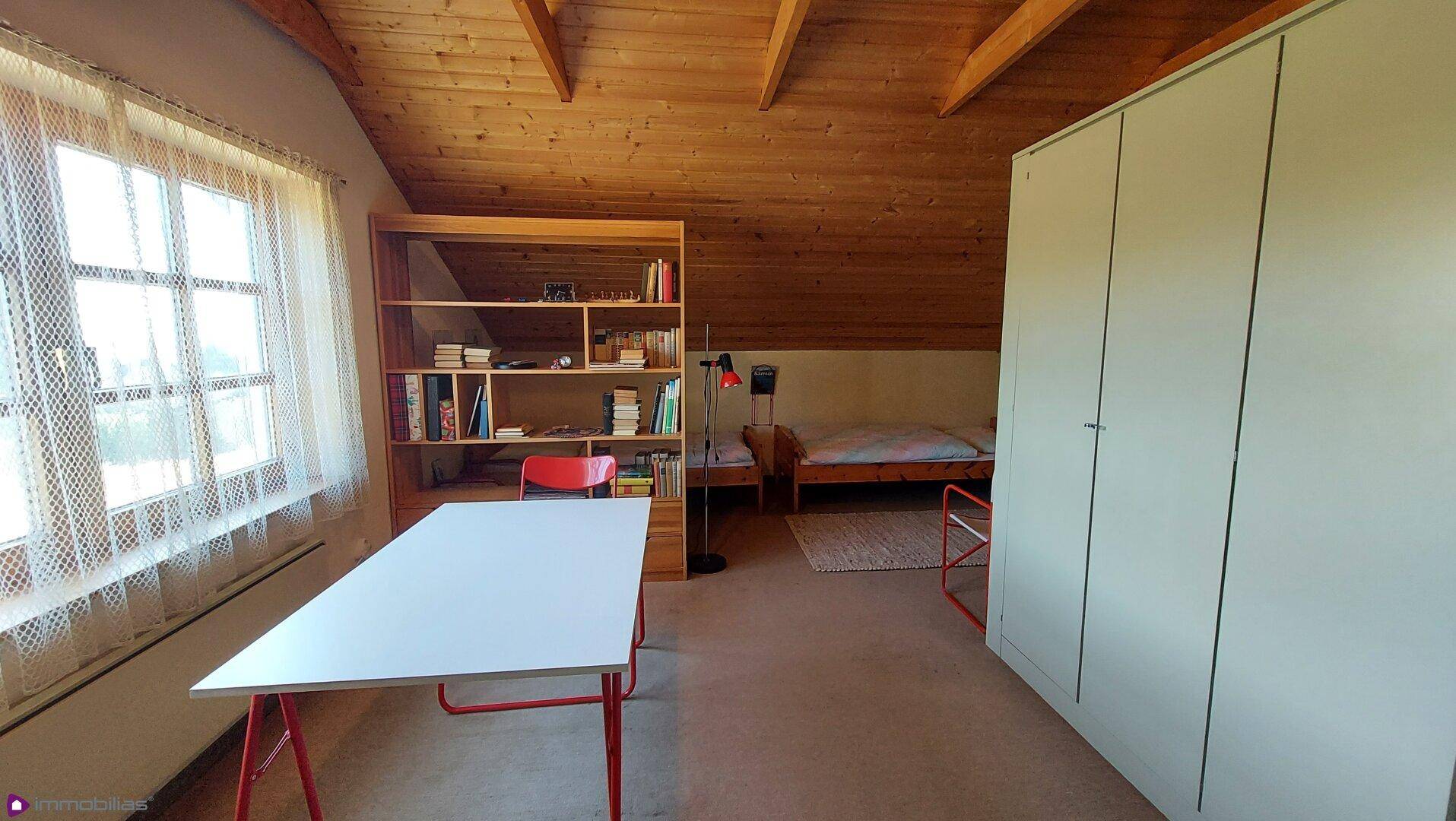Dachgeschosszimmer mit Holzbalkendecke, Schreibtisch und Bett, hell und geräumig.