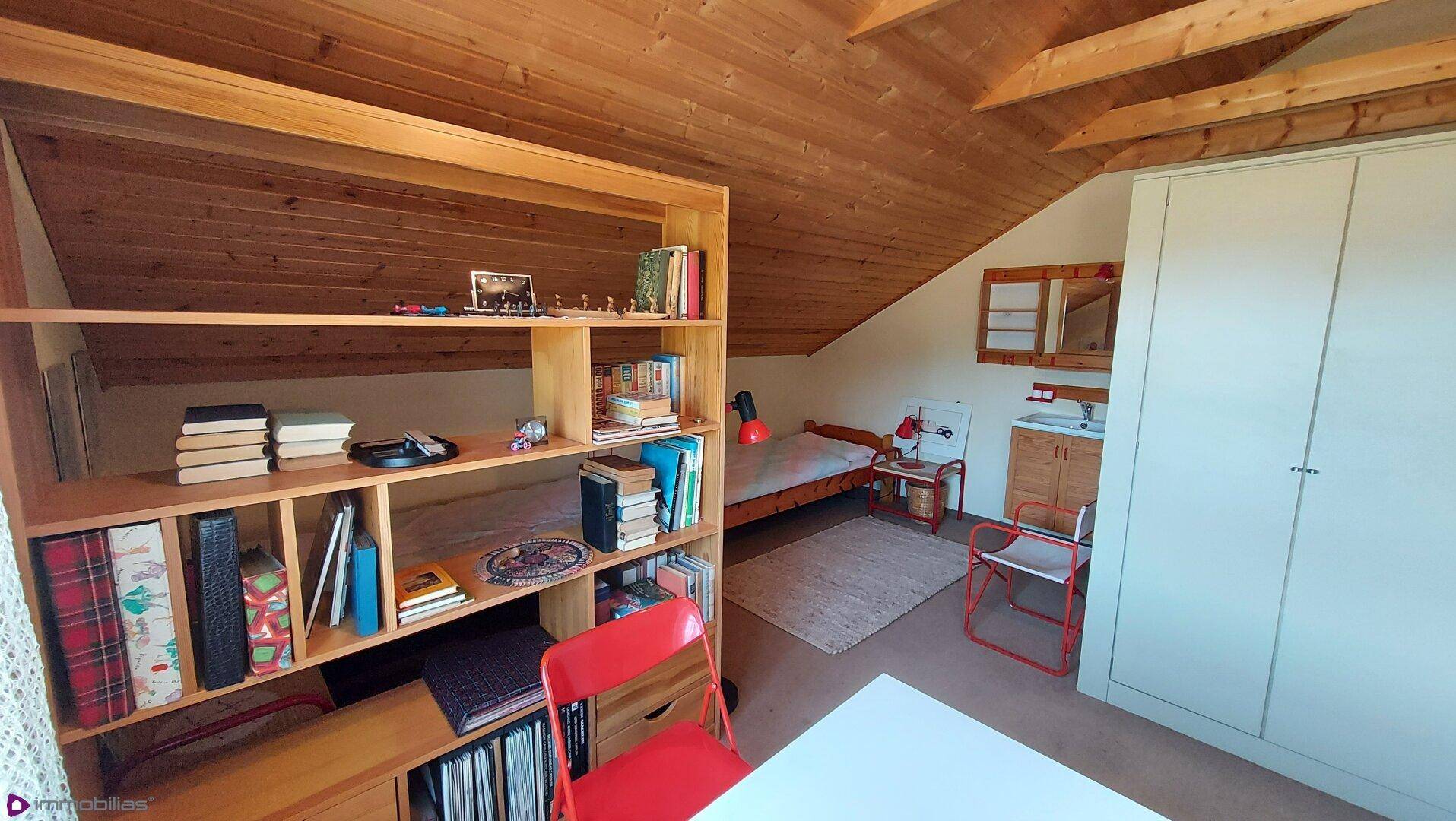 Helles Dachgeschosszimmer mit Holzbalkendecke, Regal und Bett, ideal als Gästezimmer.