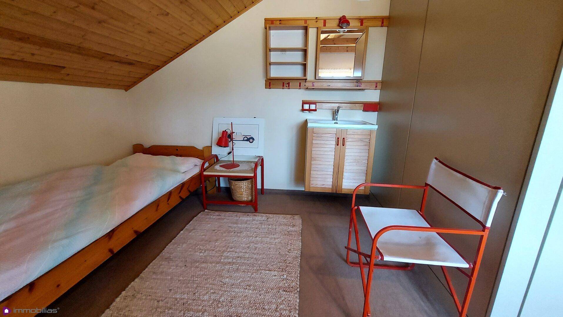 Dachgeschoss-Schlafzimmer mit Einzelbett, Holzdecke und kleinem Waschbereich.