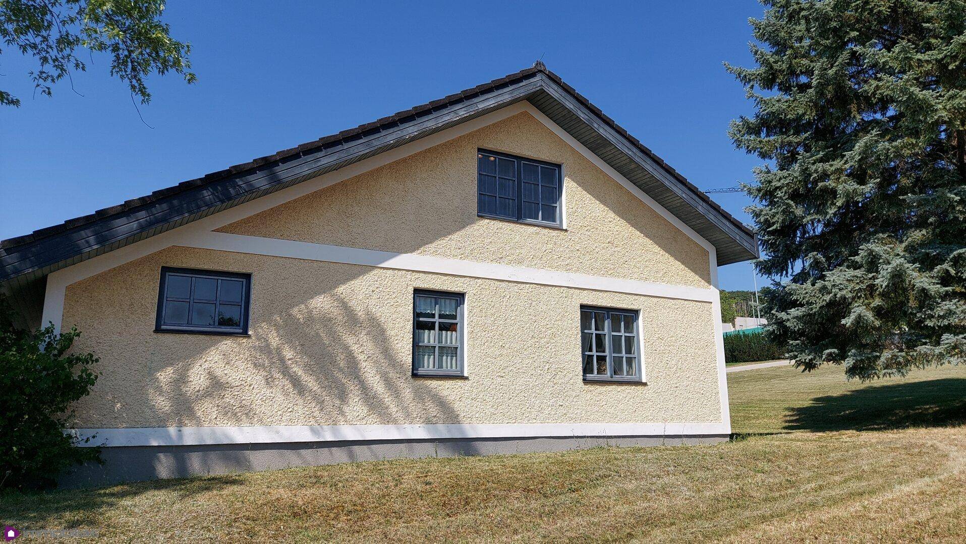 Seitenansicht eines Landhauses mit gelber Fassade und mehreren Fenstern.