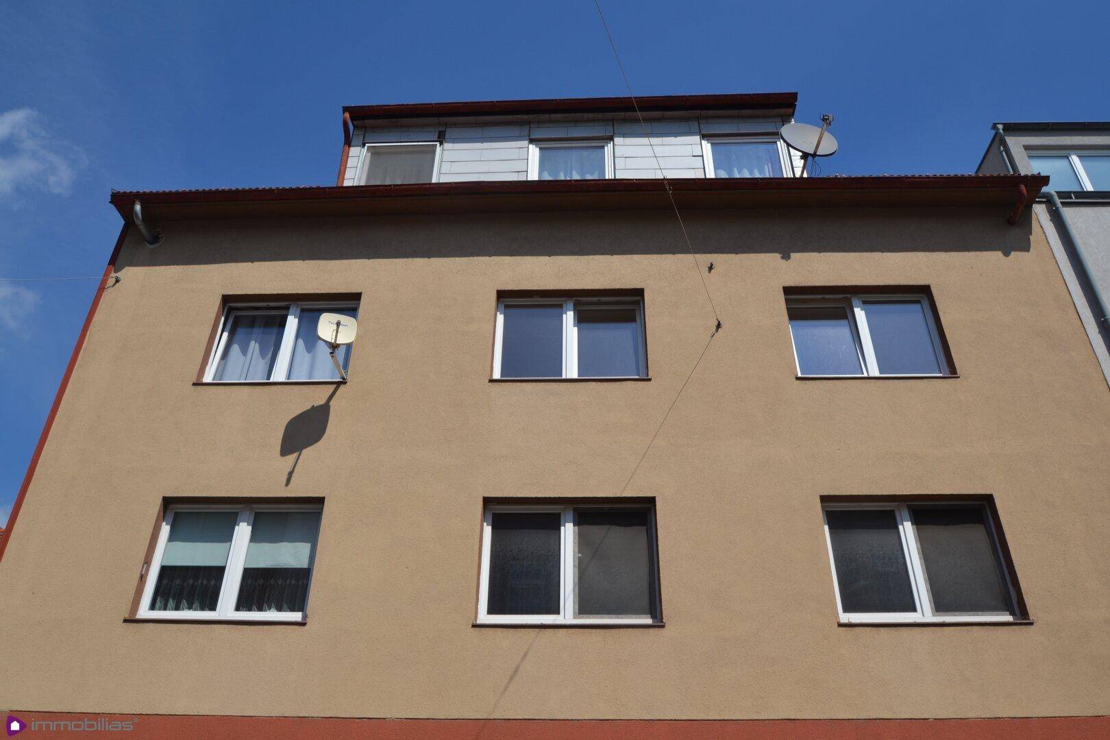 Fassade eines Mehrfamilienhauses mit mehreren Fenstern unter blauem Himmel.