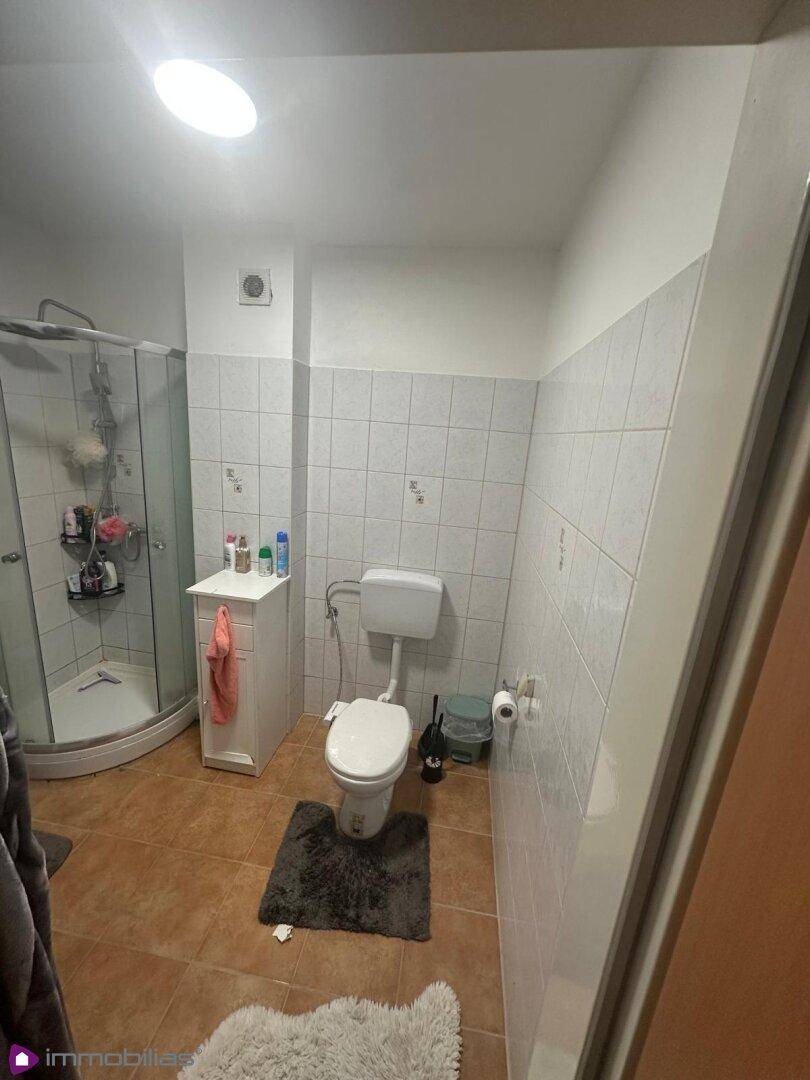 Badezimmer mit Toilette, Duschkabine und gefliesten Wänden.