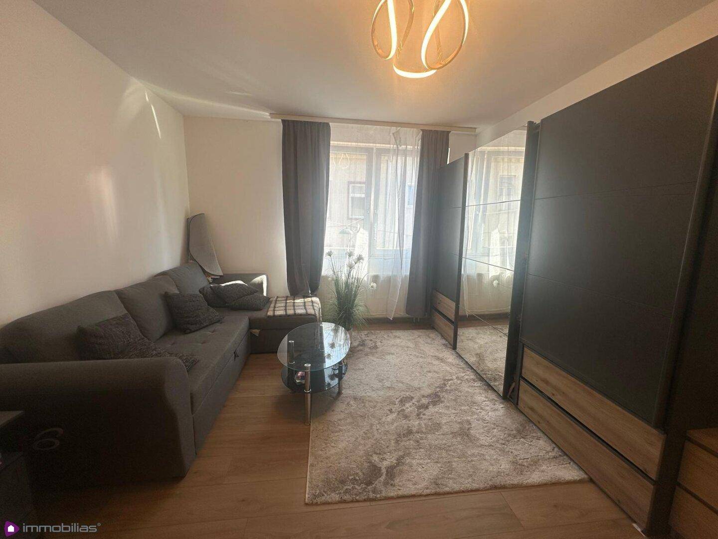 Gemütliches Wohnzimmer mit Sofa, Couchtisch und großem Spiegelschrank, hell durch Fenster.