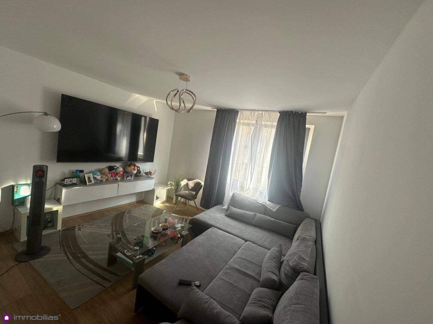 Geräumiges Wohnzimmer mit großem Ecksofa, Fernseher und viel Tageslicht.