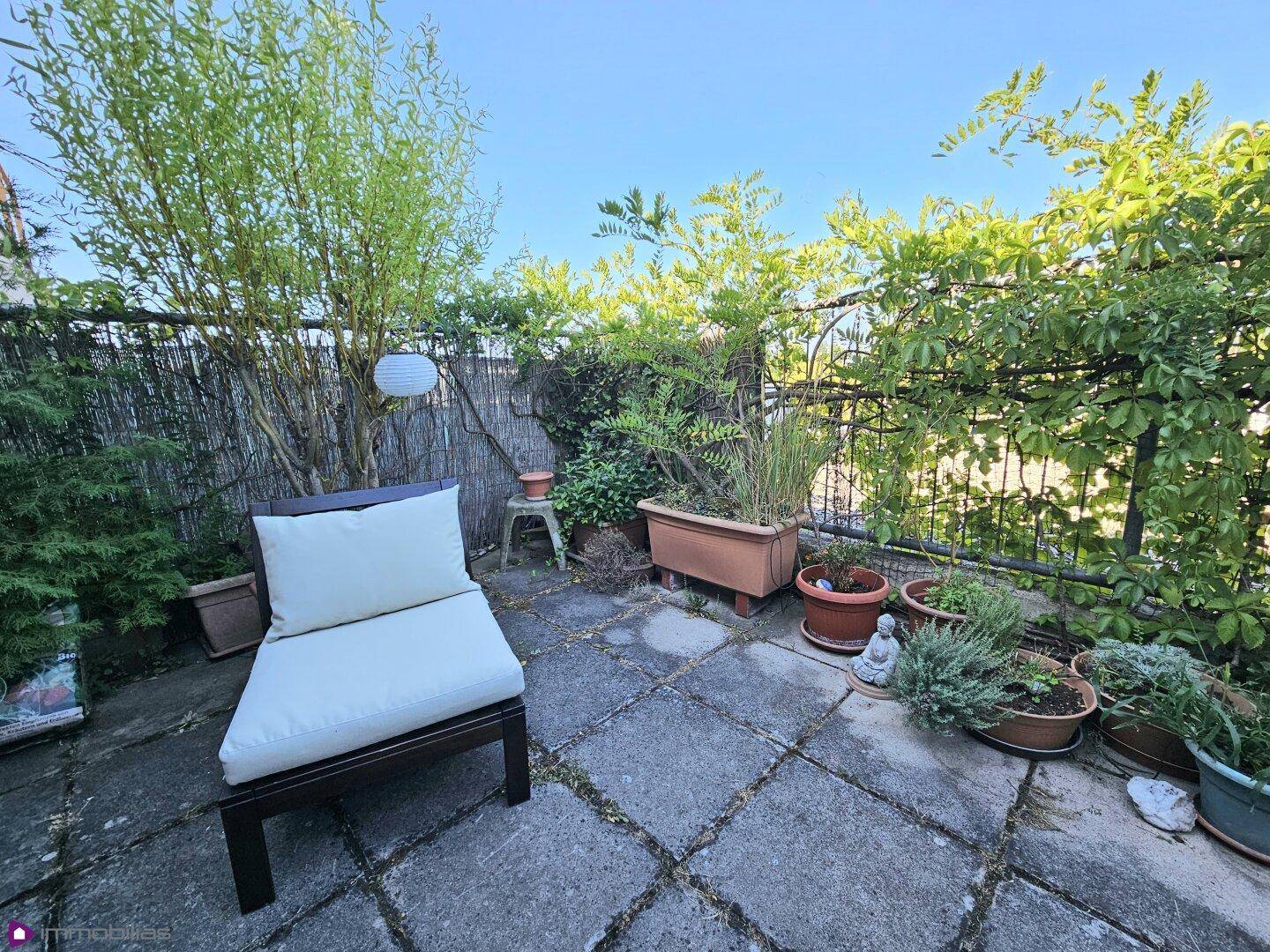 Grüne Terrasse mit Steinplatten, bepflanzten Töpfen und einem Loungesessel.