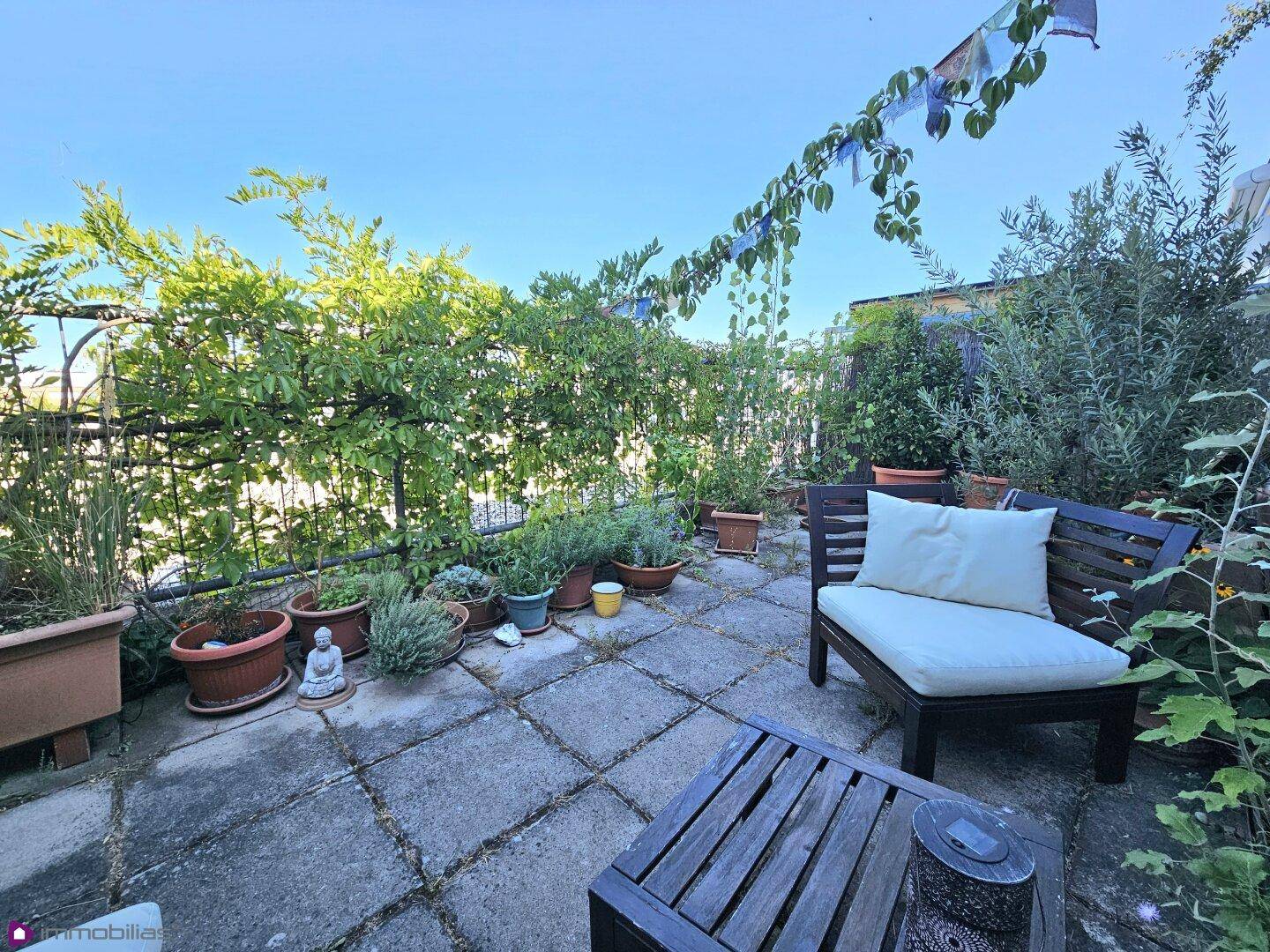 Gemütliche Terrasse mit üppiger Bepflanzung, Holztisch und Loungesessel für Entspannung.