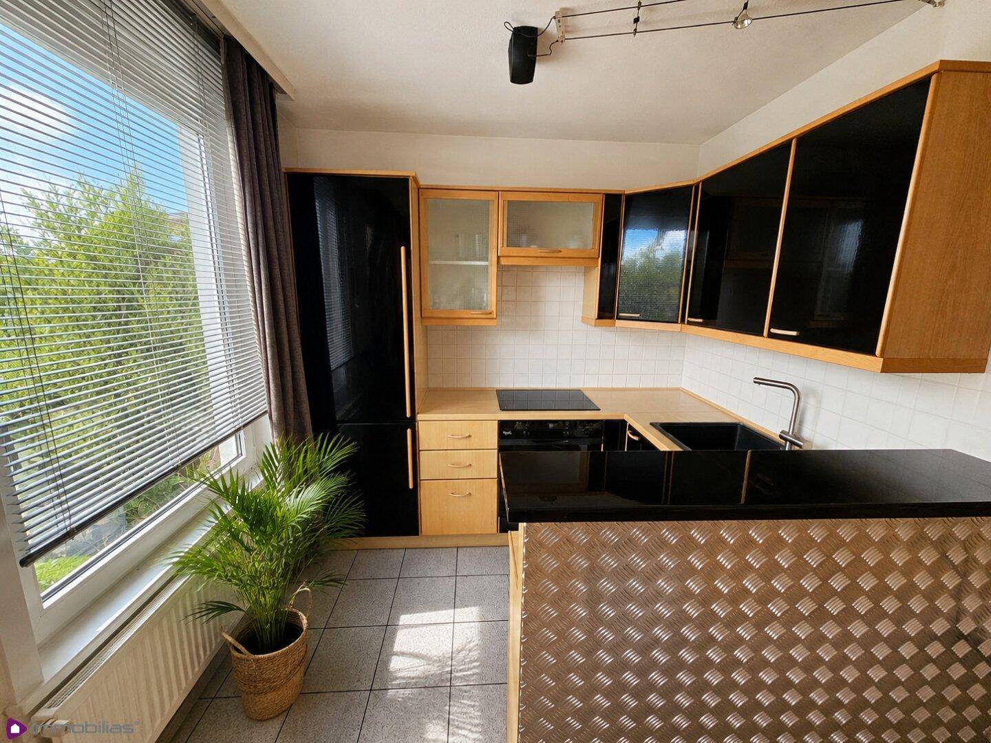 Funktionale Küche mit schwarzen und holzfarbenen Schränken, Fliesenboden und Fenster.