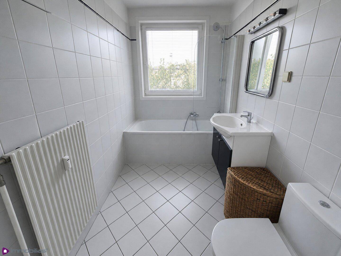 Helles Badezimmer mit weißen Fliesen, Badewanne, Waschbecken und Fenster.
