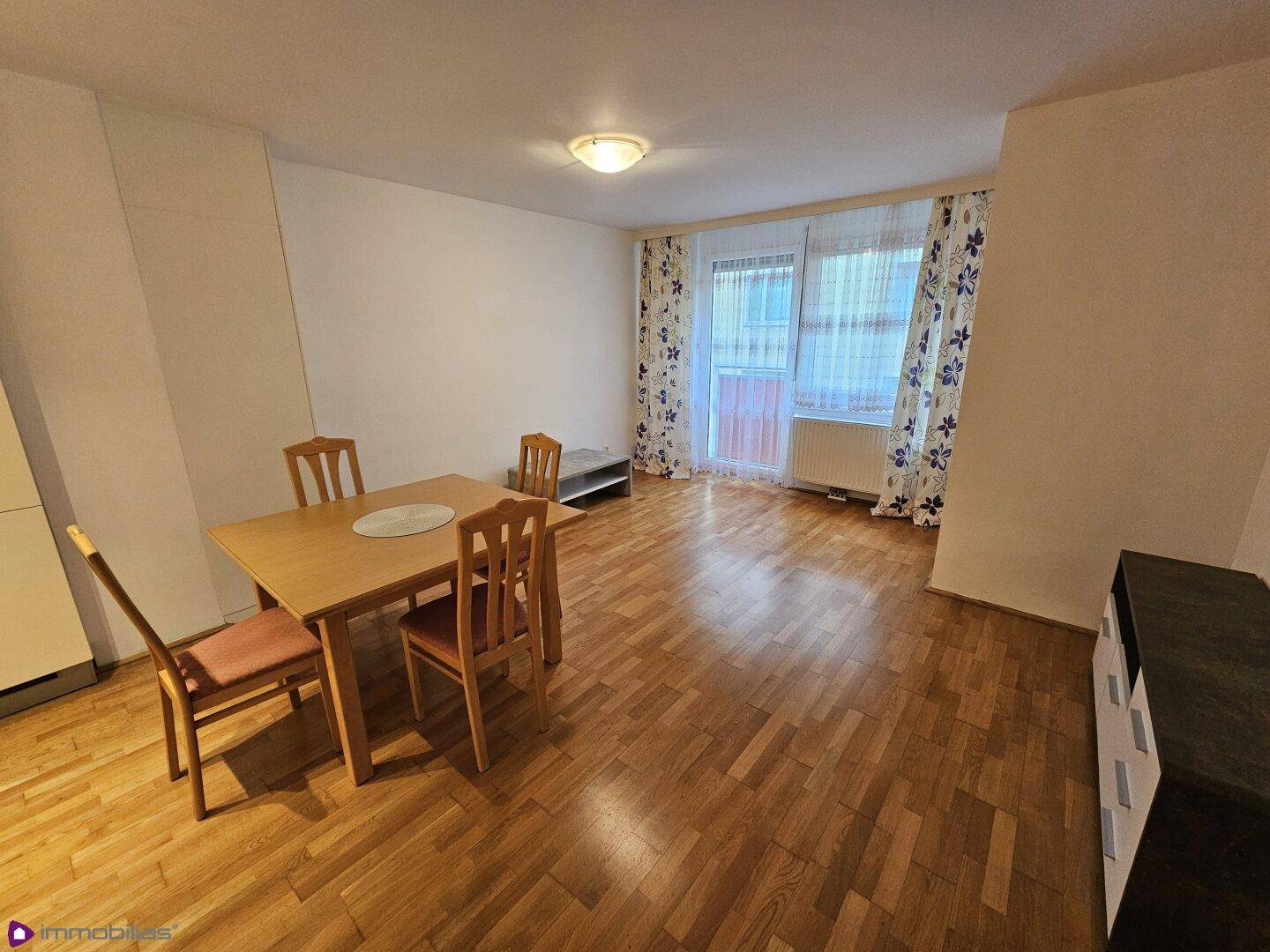 Geräumiger Wohn-Essbereich mit Holzboden, Esstisch und Zugang zu einem Balkon.