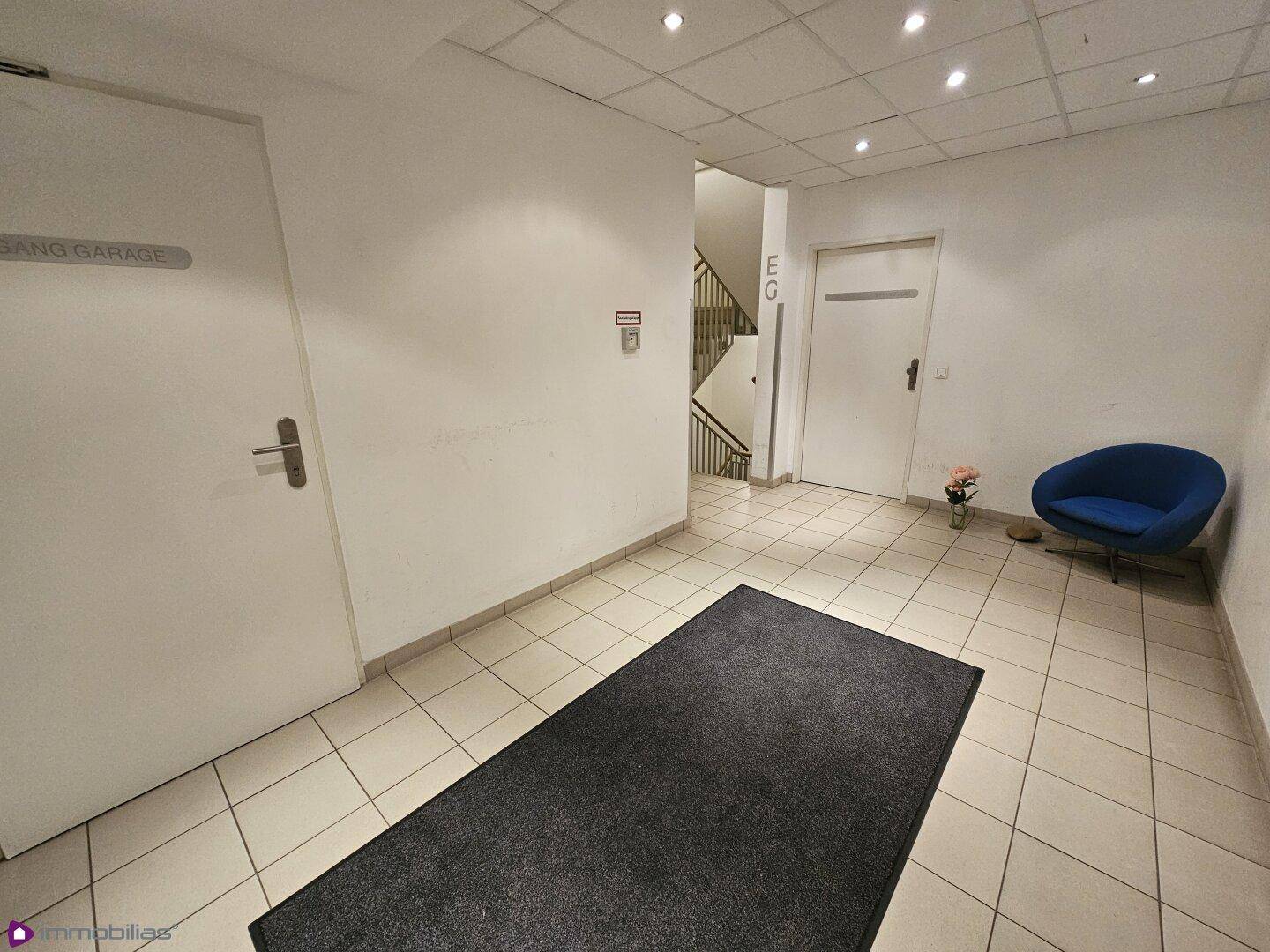 Gemeinschaftlicher Eingangsbereich mit Fliesenboden, einer blauen Sitzgelegenheit und Zugang zur Garage.