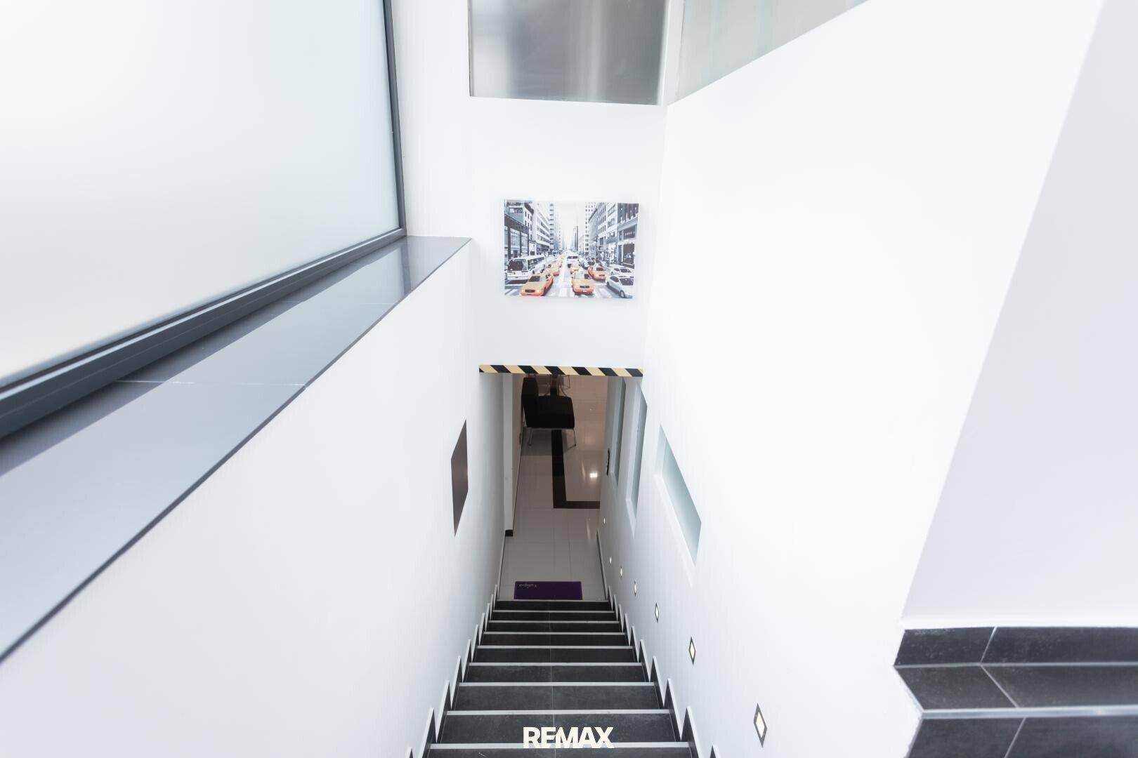 Treppenhaus mit dunklen Stufen, weißen Wänden und einem modernen Kunstwerk.