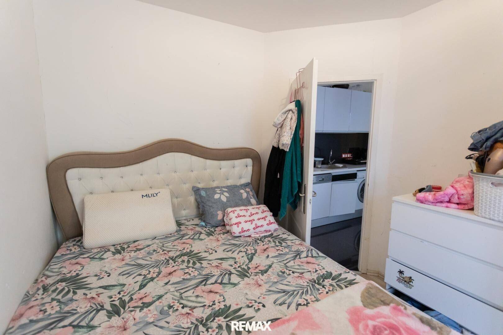 Schlafzimmer mit einem Bett, Kommode und Blick in einen angrenzenden Raum.