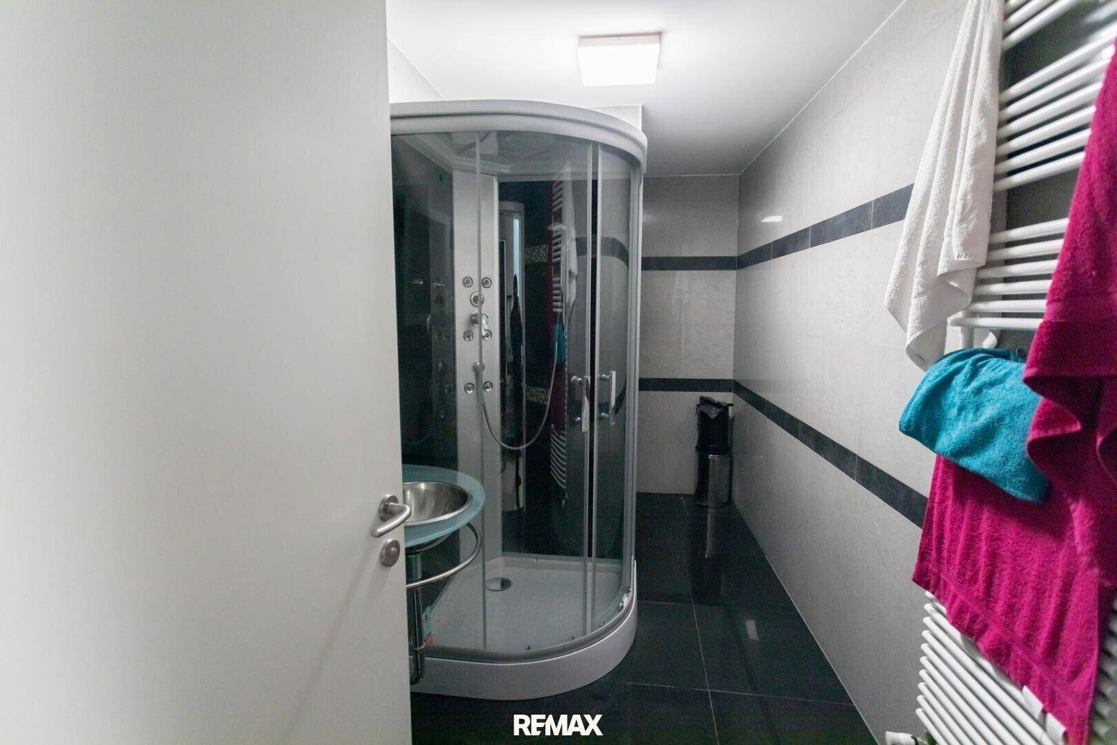 Badezimmer mit moderner Duschkabine, Waschbecken und Handtuchheizkörper.