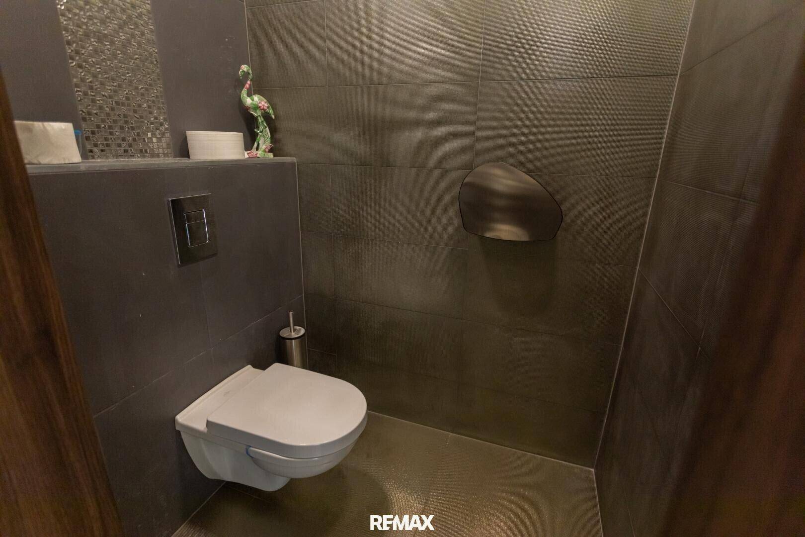 Separate Toilette mit wandhängendem WC und dunklen Fliesen an Wänden und Boden.