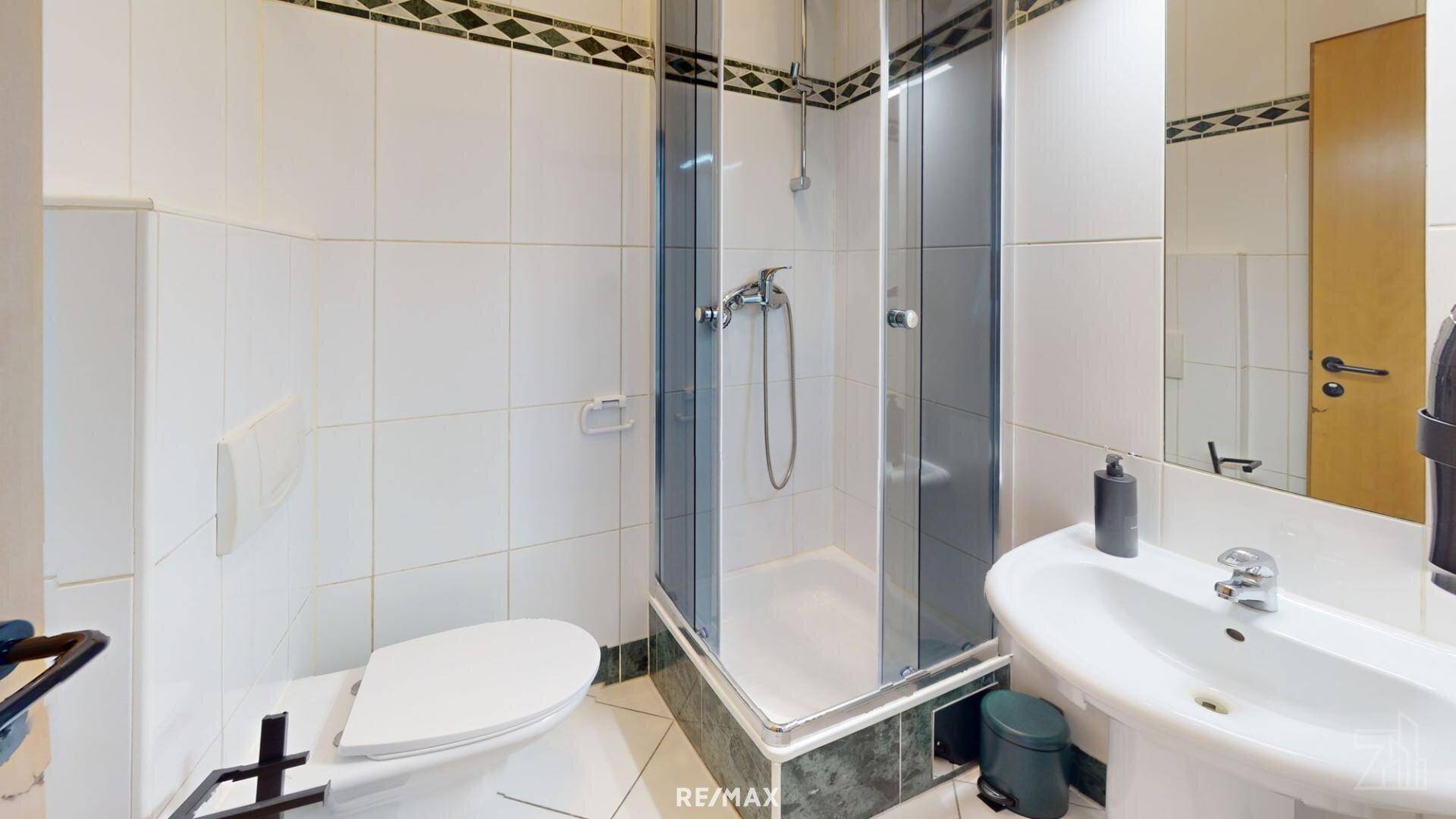 Badezimmer mit Duschkabine, WC und Waschbecken, ausgestattet mit weißen Fliesen und grünen Akzenten.