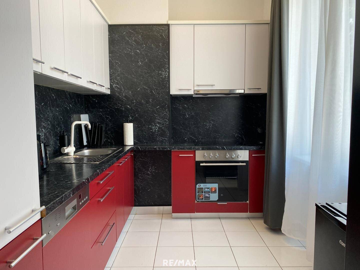 Moderne Küche mit roten Unterschränken, weißen Oberschränken und schwarzer Arbeitsplatte.