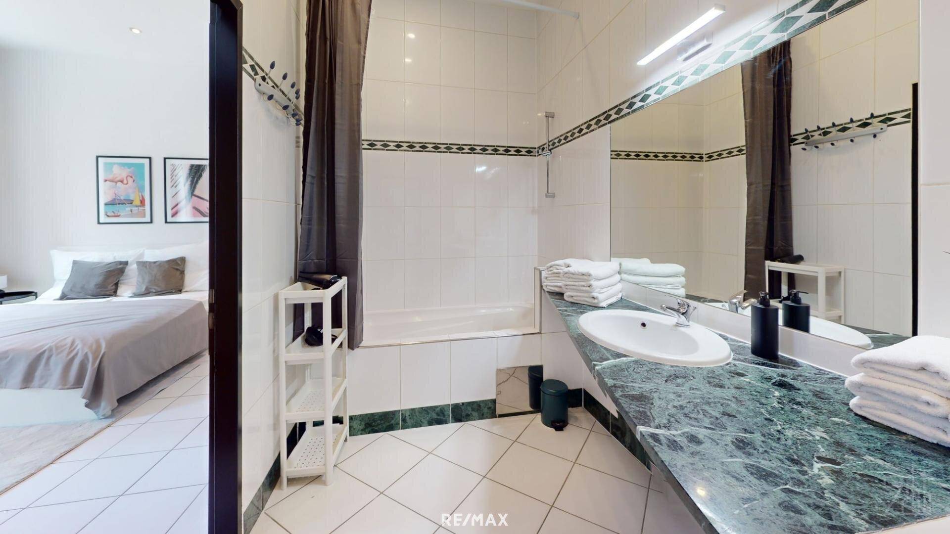 Geräumiges Badezimmer mit Badewanne, großem Waschtisch und Spiegel, direkt vom Schlafzimmer zugänglich.