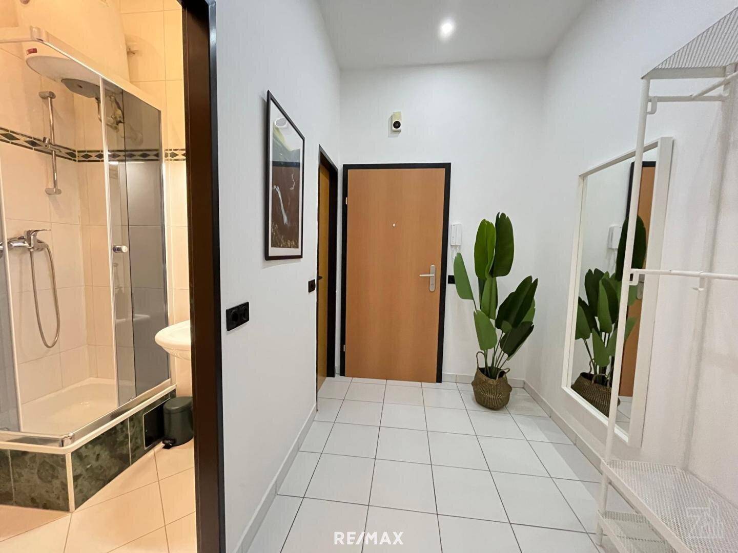 Heller Eingangsbereich mit Fliesenboden, großem Spiegel und Zugang zu weiteren Räumen.