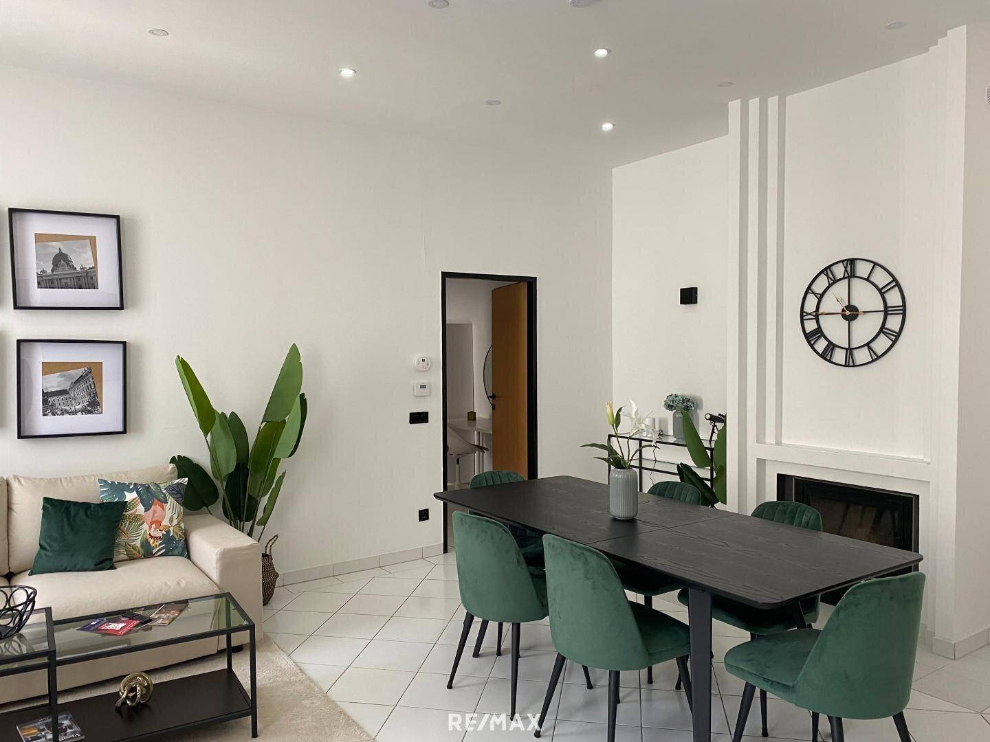 Offener Wohn- und Essbereich mit modernem Esstisch, grünen Stühlen und einem dekorativen Kamin.