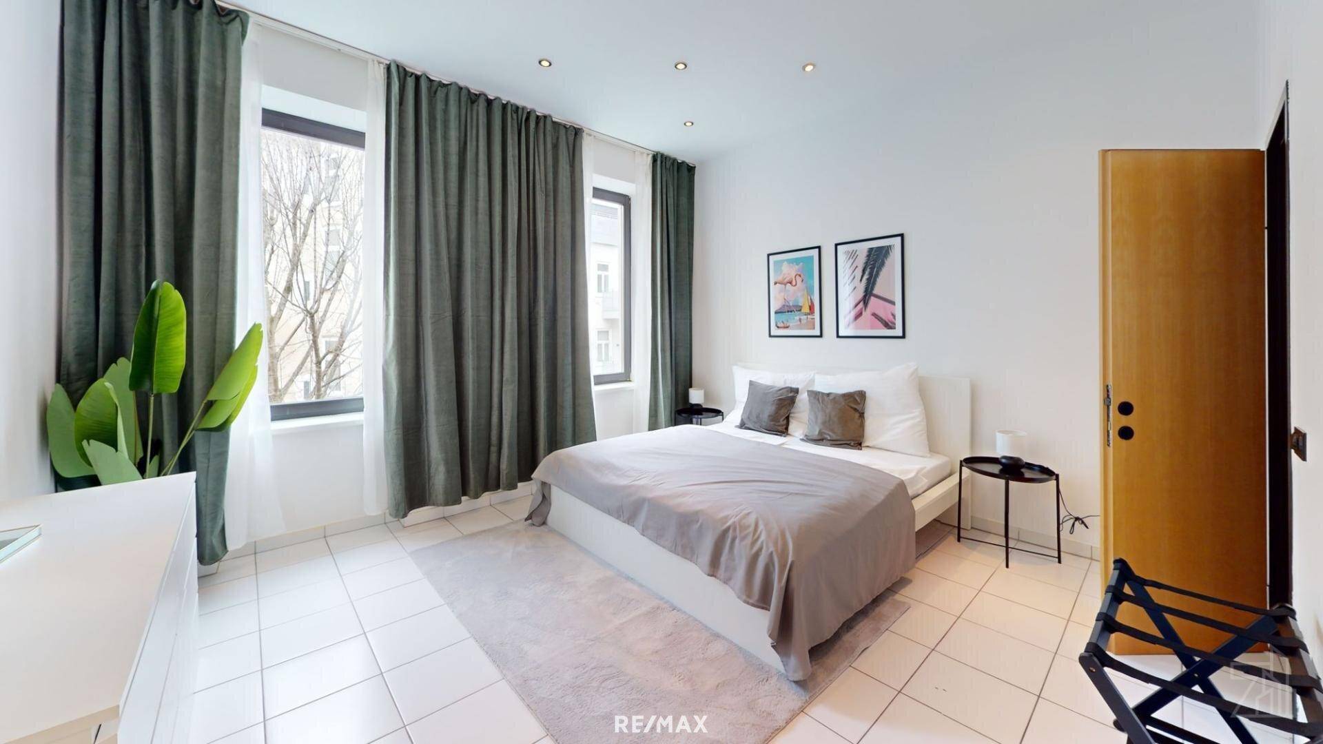 Großes Schlafzimmer mit Doppelbett, hohen Fenstern und schlichten, dunklen Vorhängen.