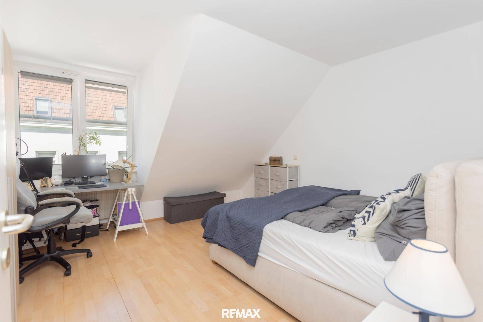 Helles Schlafzimmer mit Bett, Schreibtisch und Fenster unter der Dachschräge.