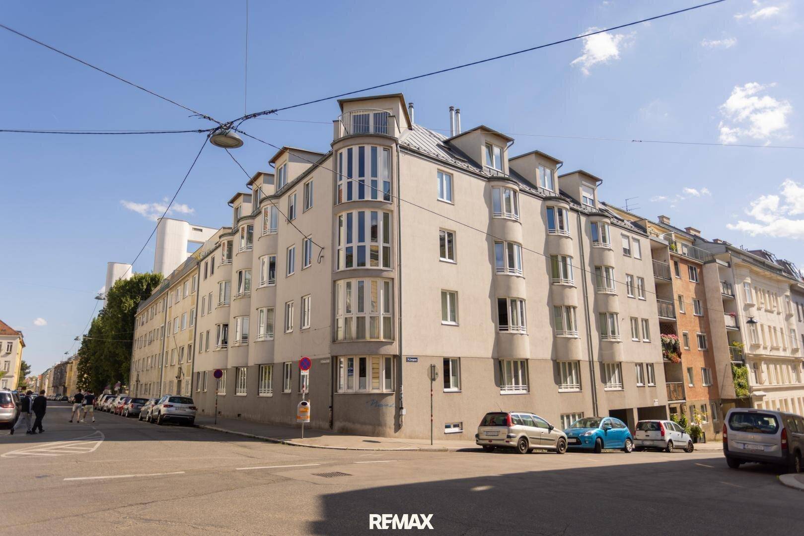 Attraktives Eckgebäude mit vielen Fenstern und Mansarddach in städtischer Umgebung.
