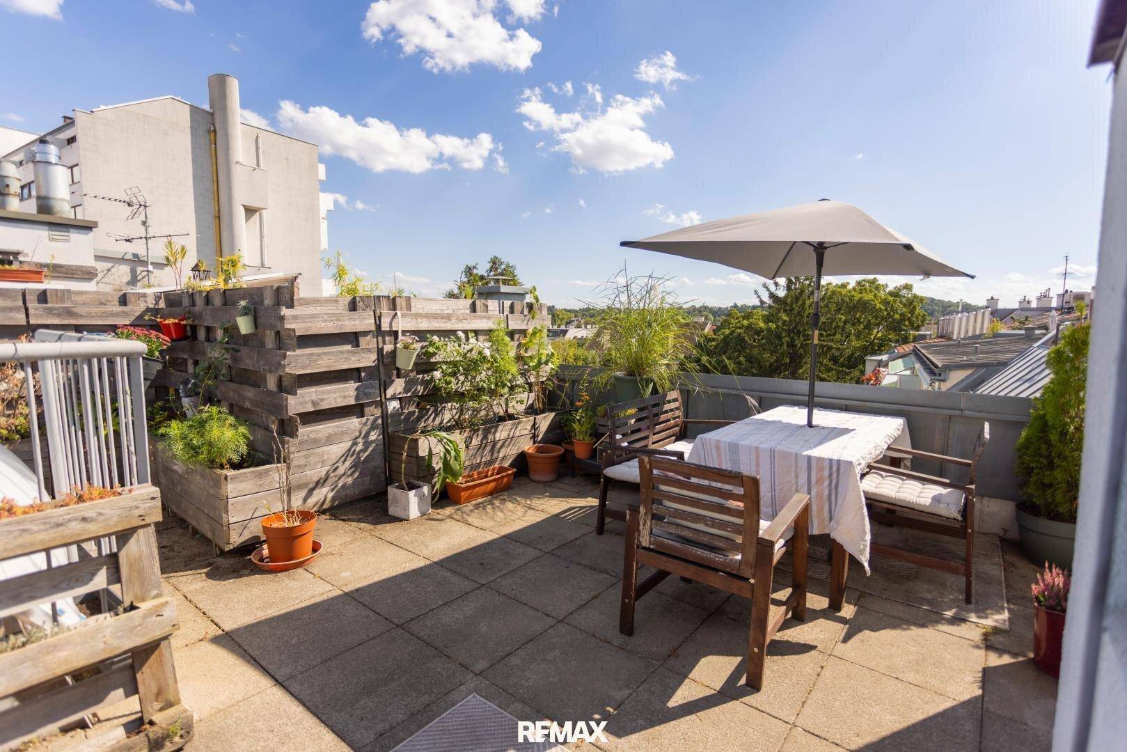 Helle Dachterrasse mit Essbereich, Sonnenschirm und vertikalem Garten an der Holzverkleidung.