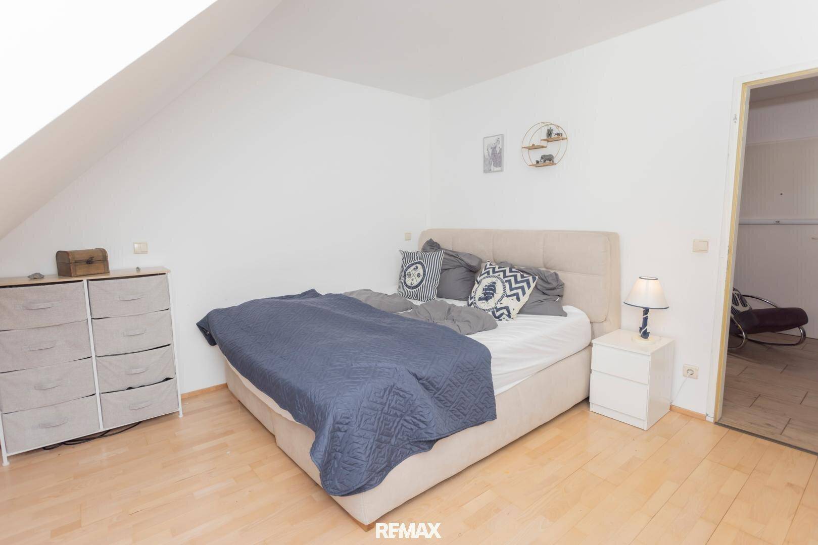 Schlafzimmer mit Doppelbett, Kommode und hellem Holzboden unter einer Dachschräge.