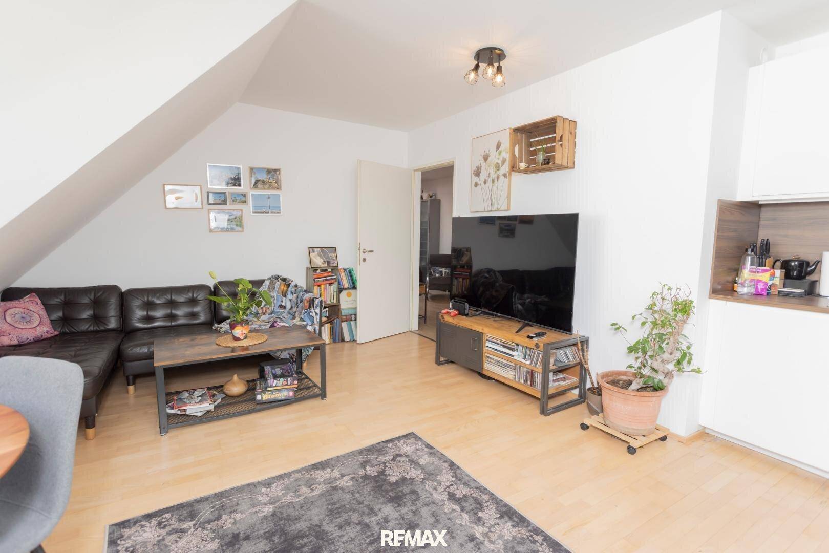 Gemütlicher Wohnbereich mit Sofa, Fernseher und Zugang zur Küche im Dachgeschoss.
