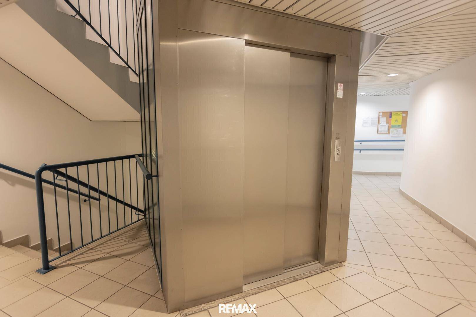 Moderner Aufzug in einem Gemeinschaftsbereich neben einer Treppe.
