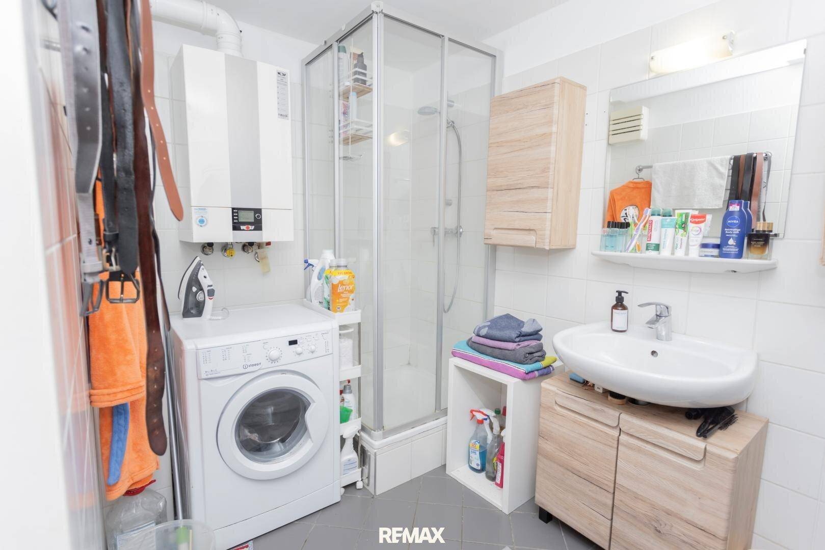 Funktionales Badezimmer mit Duschkabine, Waschmaschine und Warmwasserbereiter.