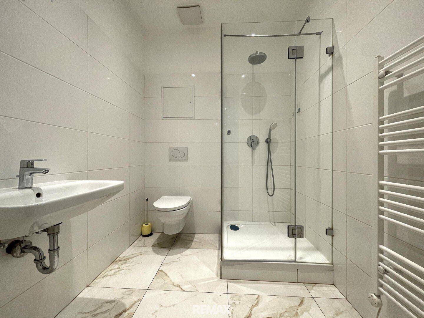 Modernes Badezimmer mit weißen Fliesen, Duschkabine, wandhängendem WC und Handtuchheizkörper.