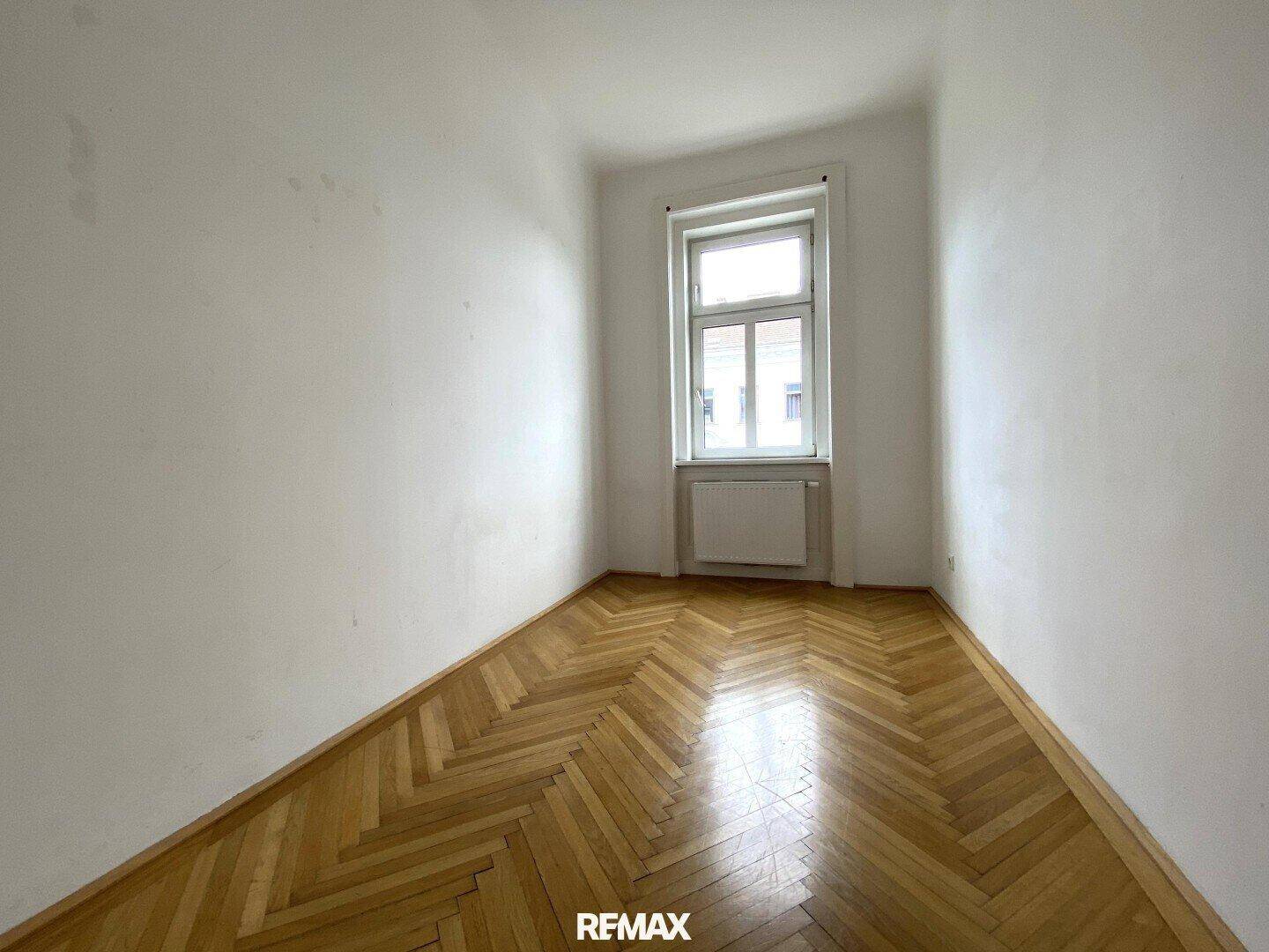Kleineres Zimmer mit hellem Fischgrätparkett, weißen Wänden und einem Fenster, ideal als Schlaf- oder Arbeitszimmer.