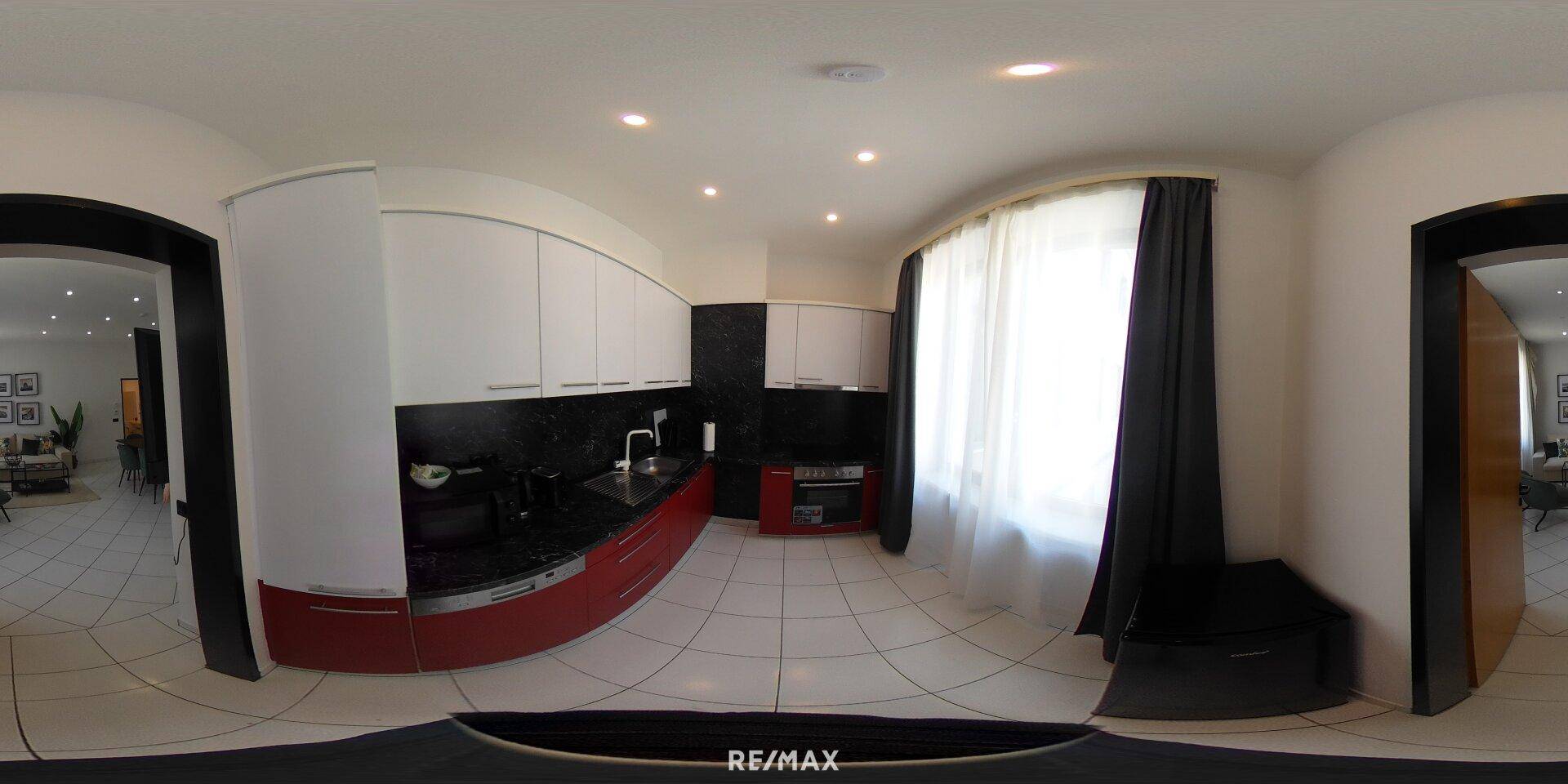 Panoramablick auf die moderne Küche mit roten und weißen Schränken und schwarzer Arbeitsplatte.