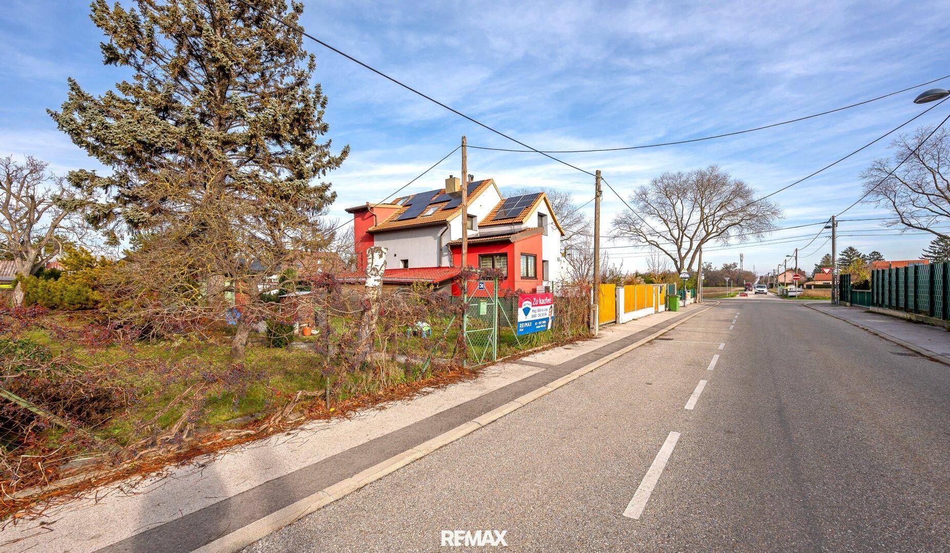 Ansicht des Hauses von der Straße mit Photovoltaikanlage auf dem Dach und umliegender Natur.