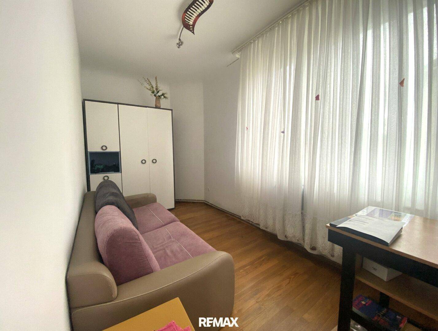 Gemütliches Wohnzimmer mit Holzparkett, einem Sofa und einem Kleiderschrank neben dem Fenster.