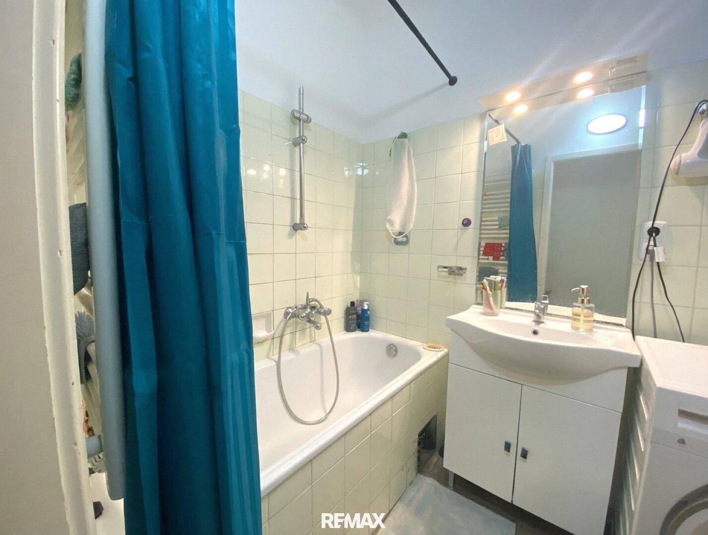 Badezimmer mit Badewanne, Duschvorhang, Waschbecken und Waschmaschine, ausgestattet mit hellgrünen Fliesen.